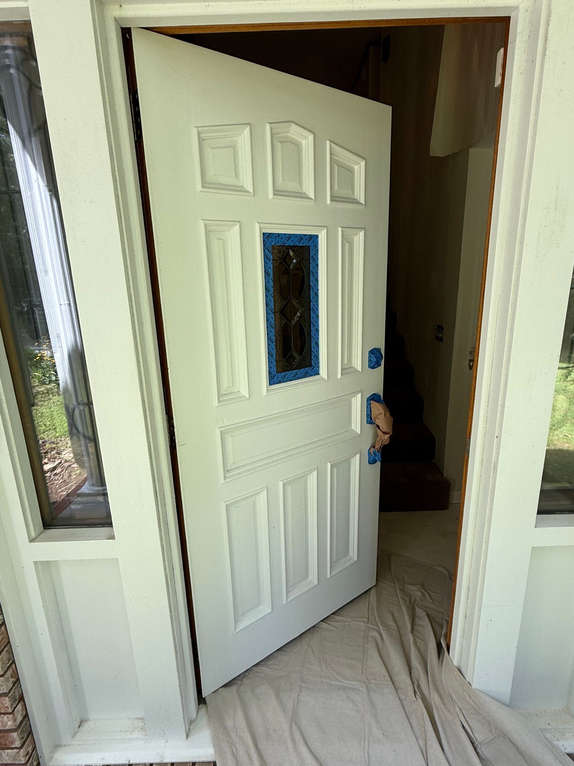 White painted door with blue tape, open, showing a hallway, tarp on the floor.
