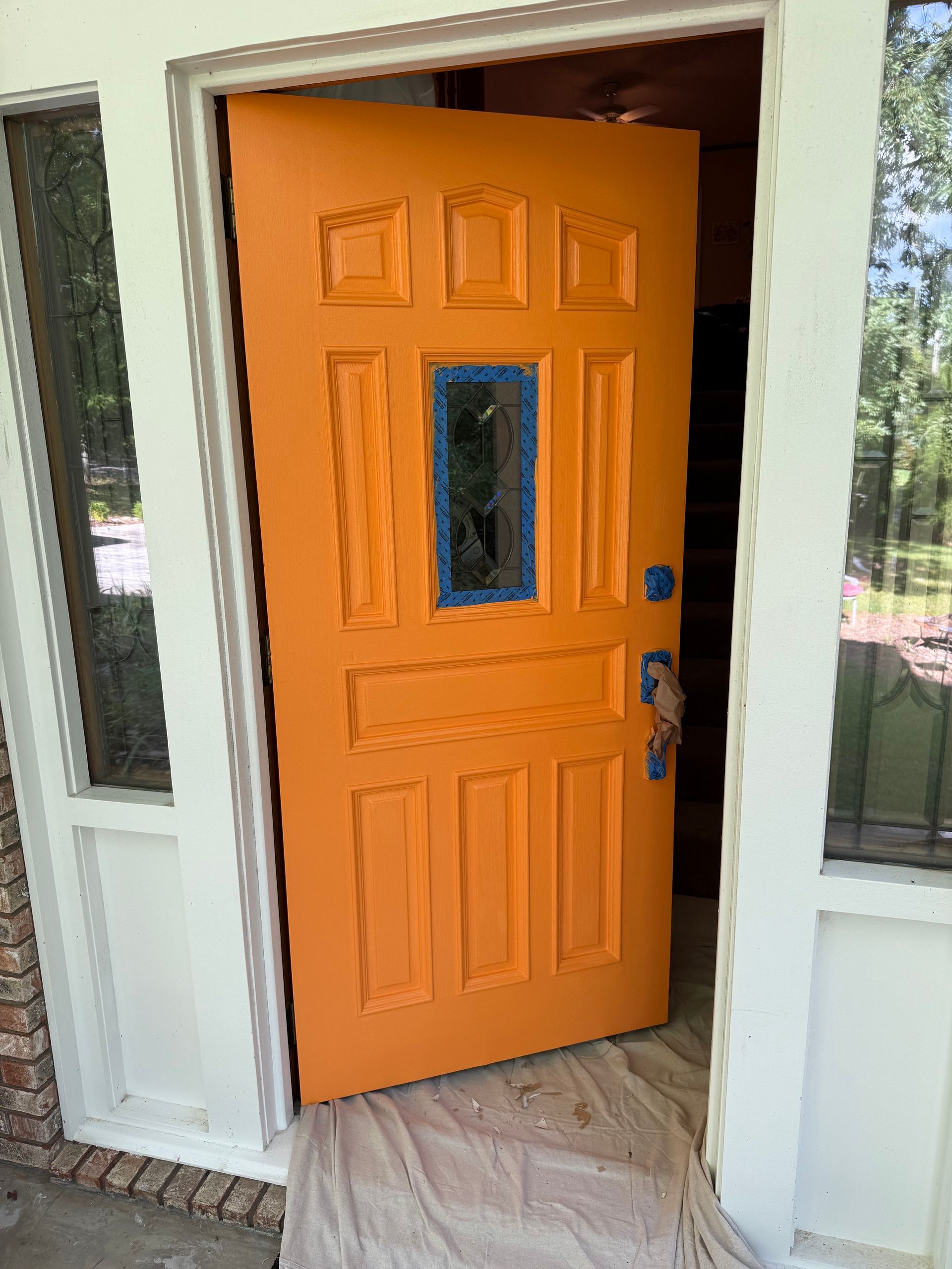 Orange painted front door slightly ajar, door frame and window trim are white.