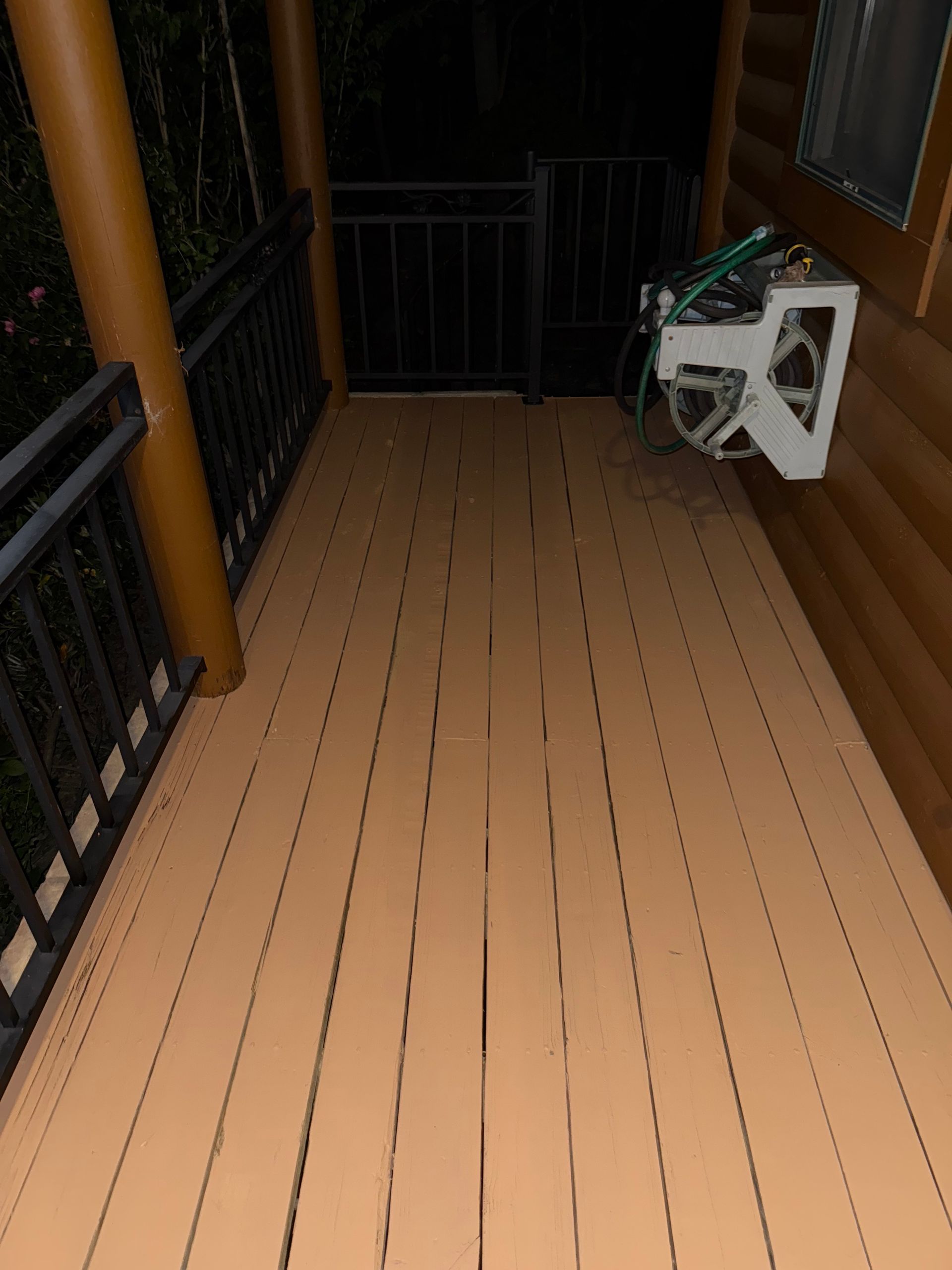Wooden porch at night with metal railing and hose reel.