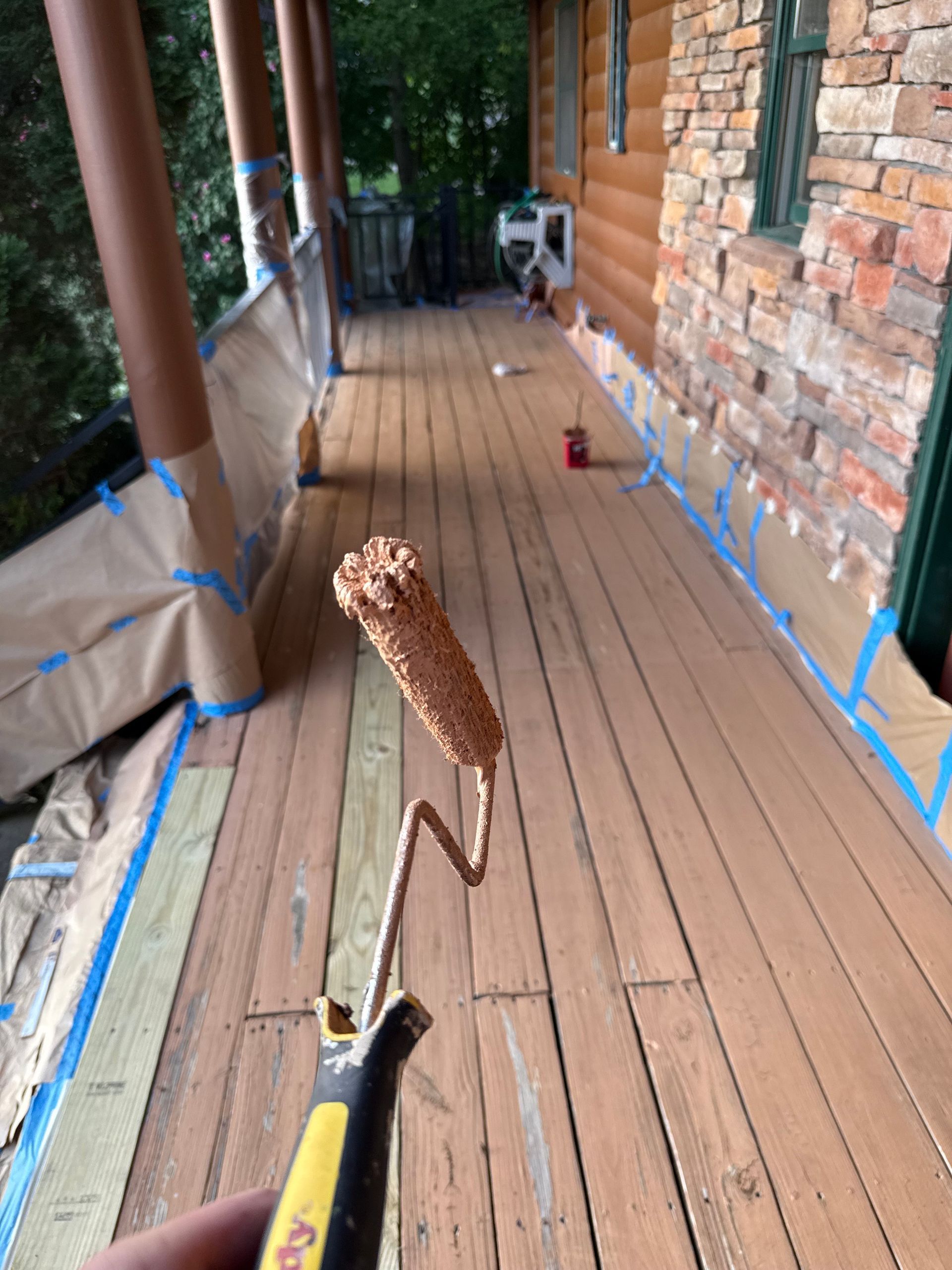 Person holding paint roller on a wooden deck, ready to paint. The deck is taped off and ready.