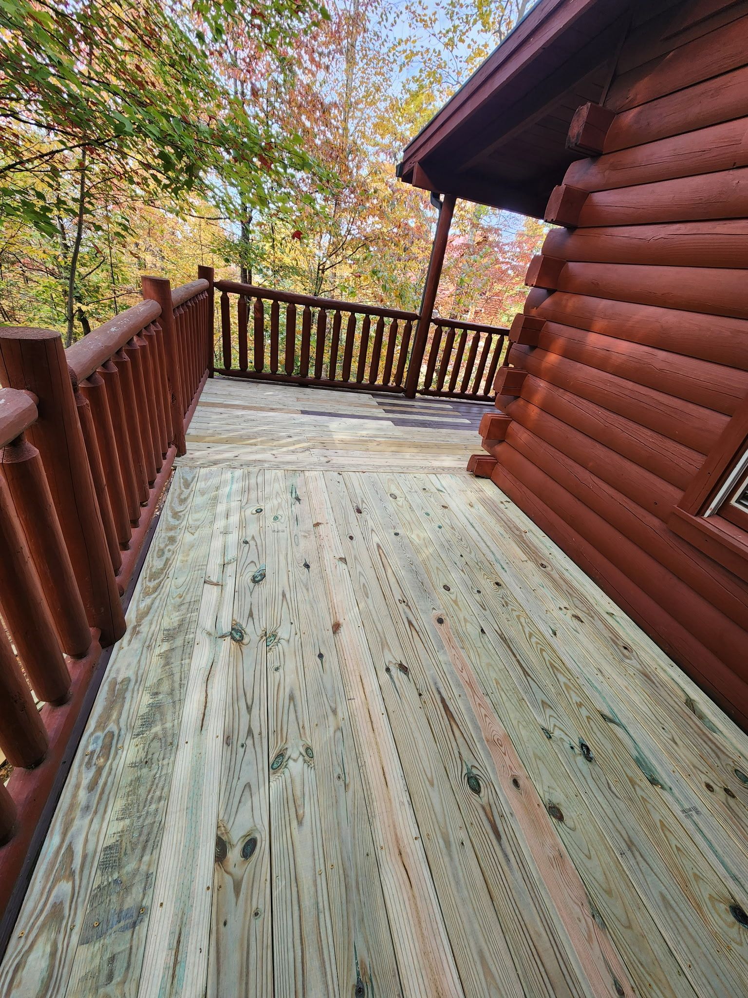 Wooden deck with railing next to a log cabin, surrounded by autumn foliage.