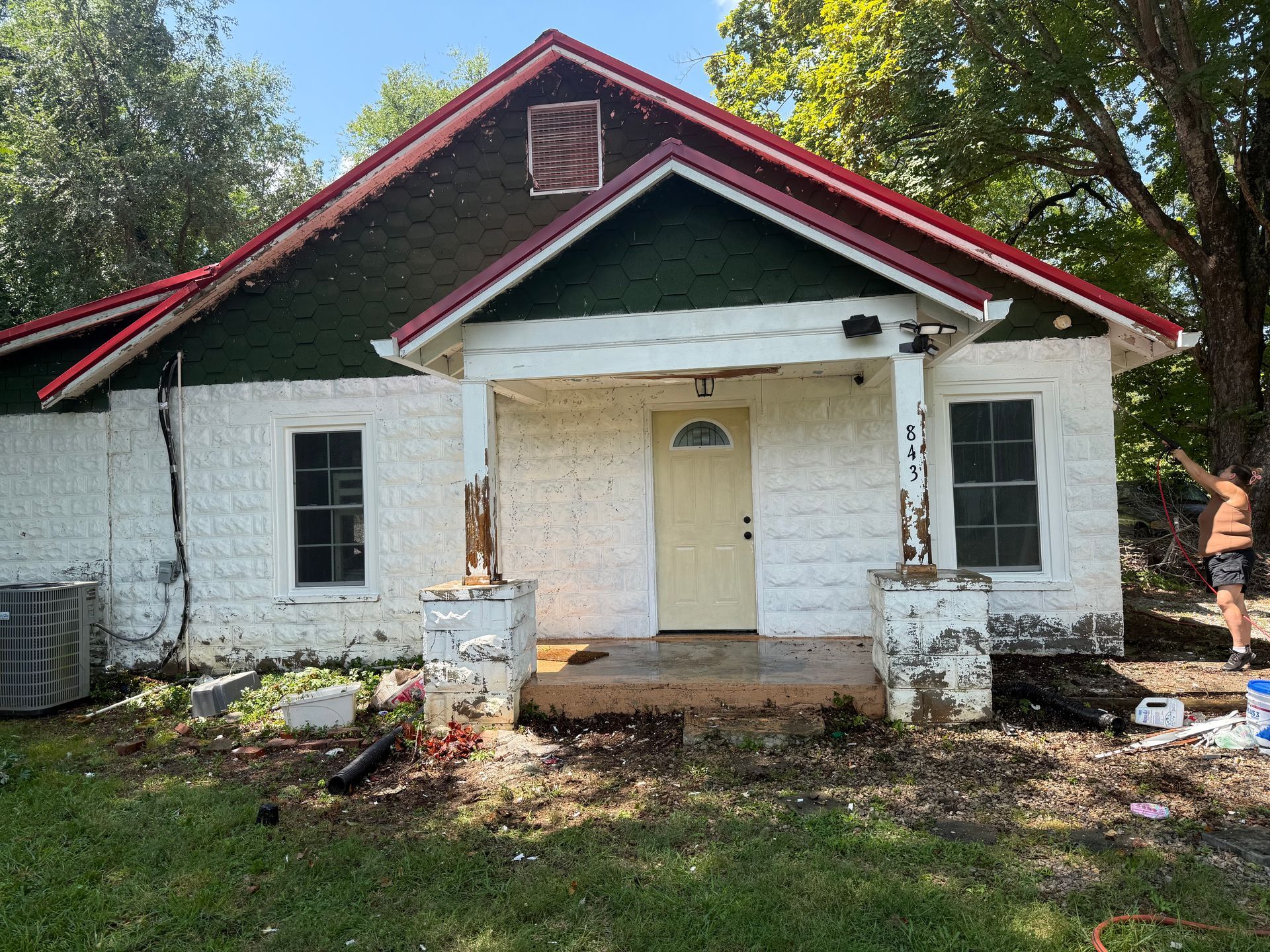 White house with red roof, porch. Person outside, greenery in yard.