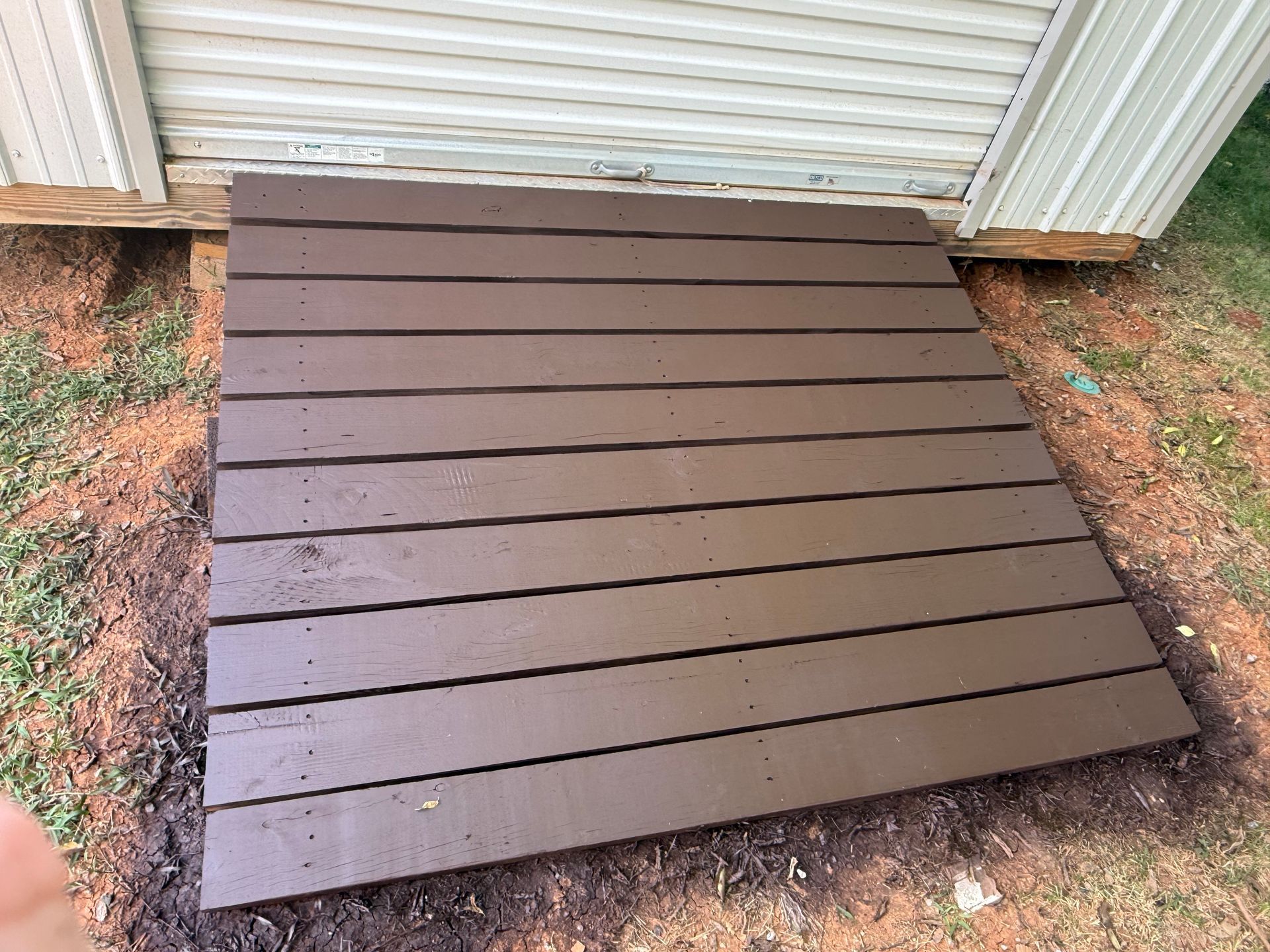Brown wooden ramp at a shed entrance, resting on dirt.