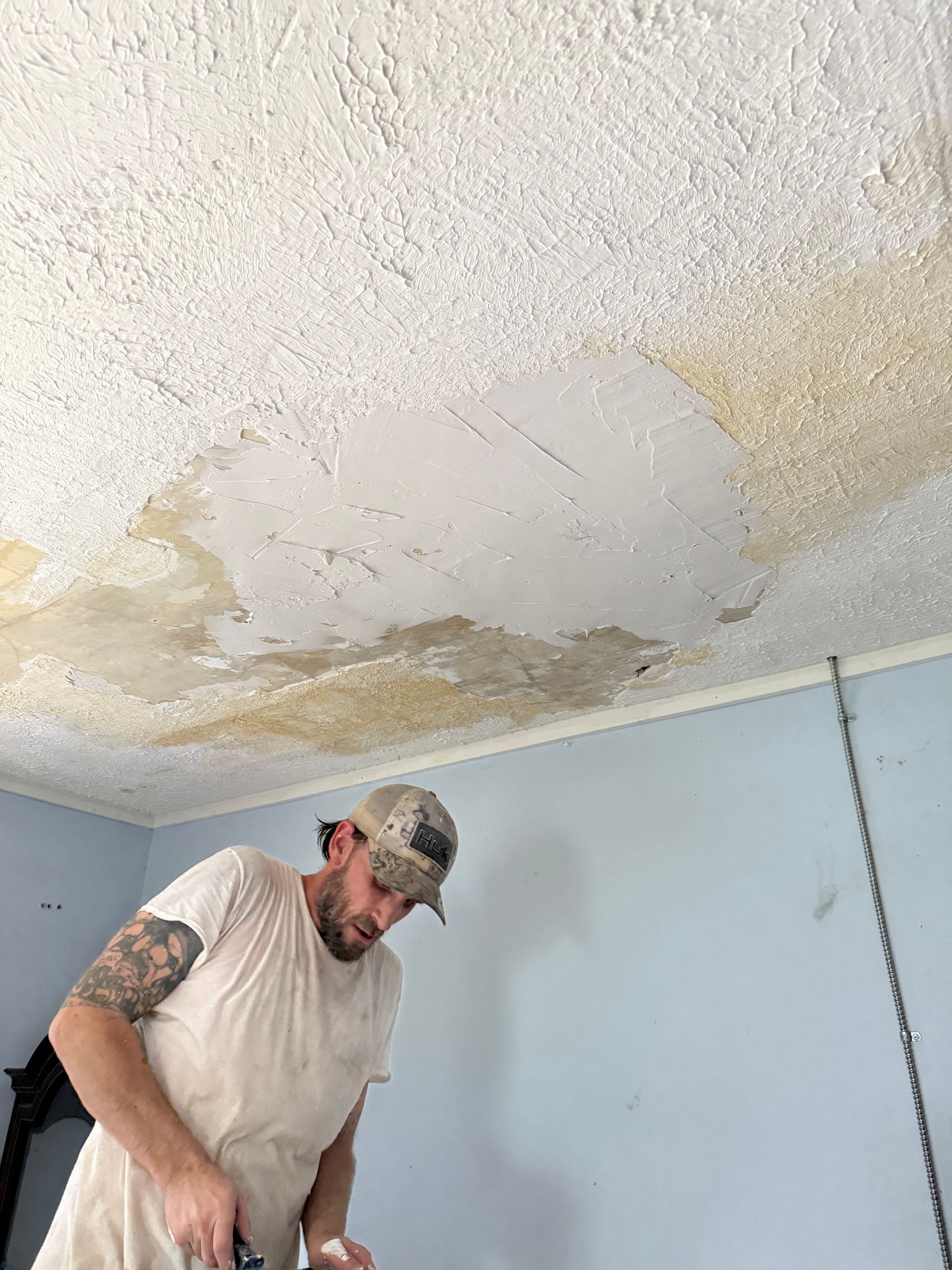 Man repairs a water-damaged textured ceiling in a room with blue walls.