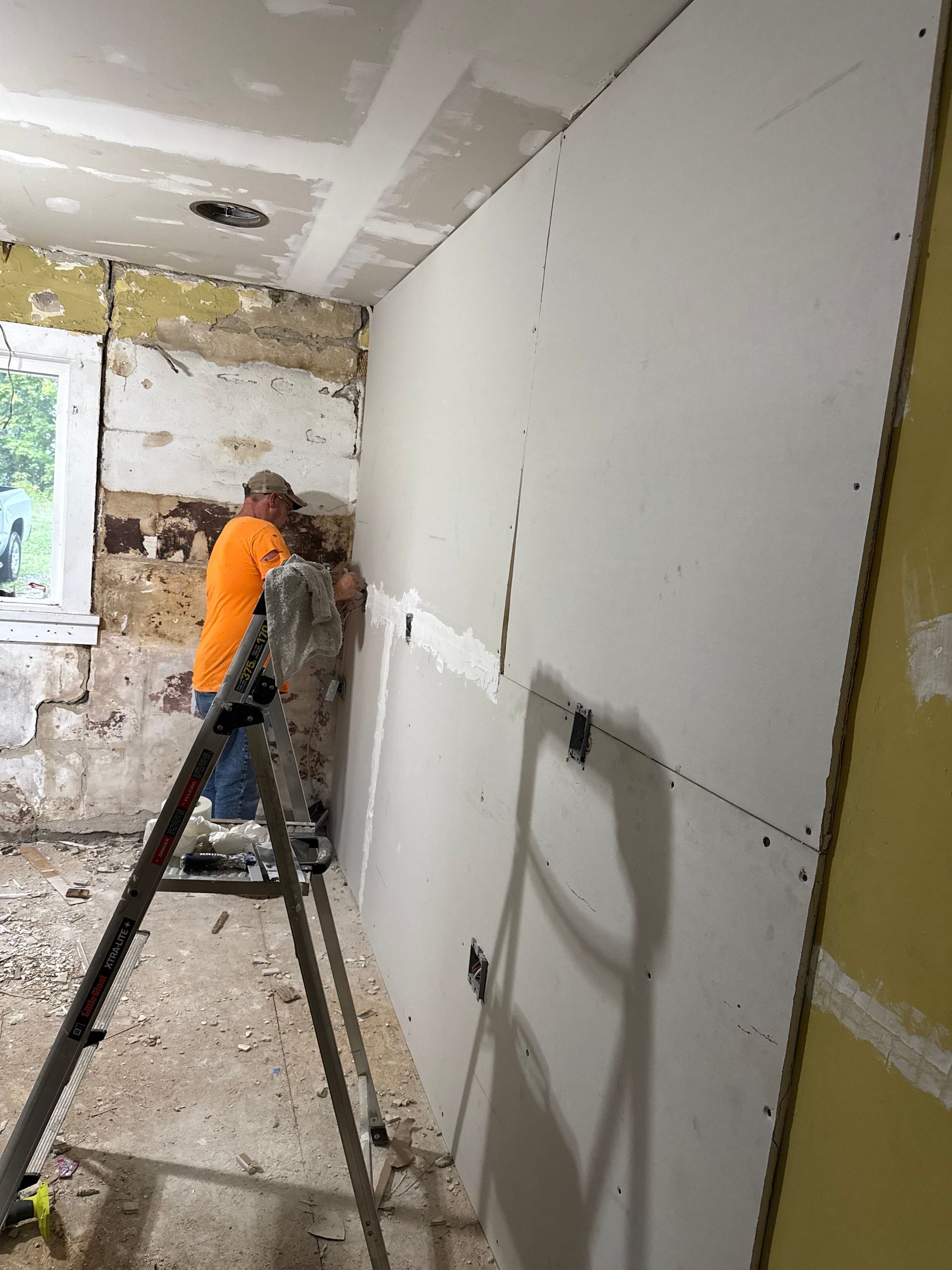 Two people installing drywall on a wall. Ladder present. Construction setting, interior.