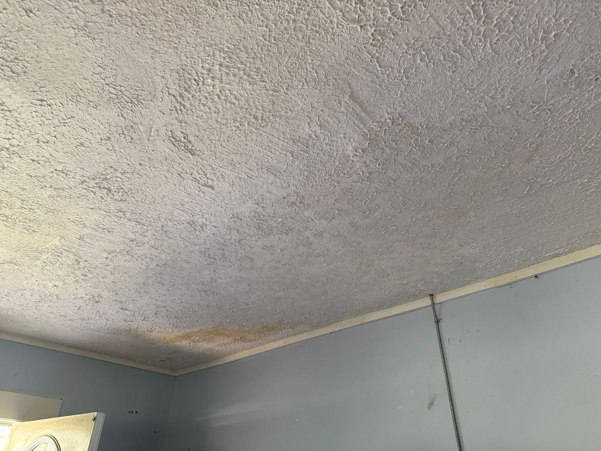 Textured white ceiling with water damage and light blue walls.