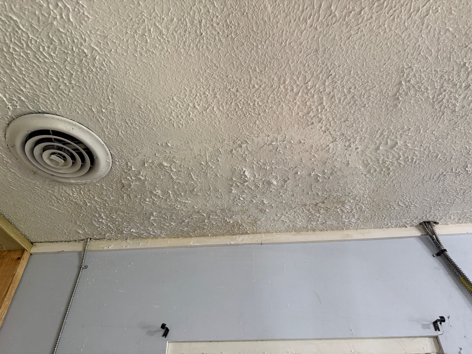 Textured, white ceiling with peeling paint, air vent, and light blue wall.