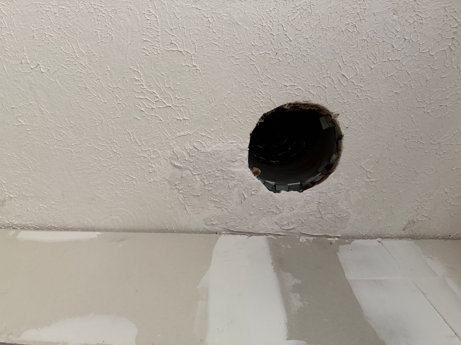 Hole in a white textured ceiling, with fresh drywall below.