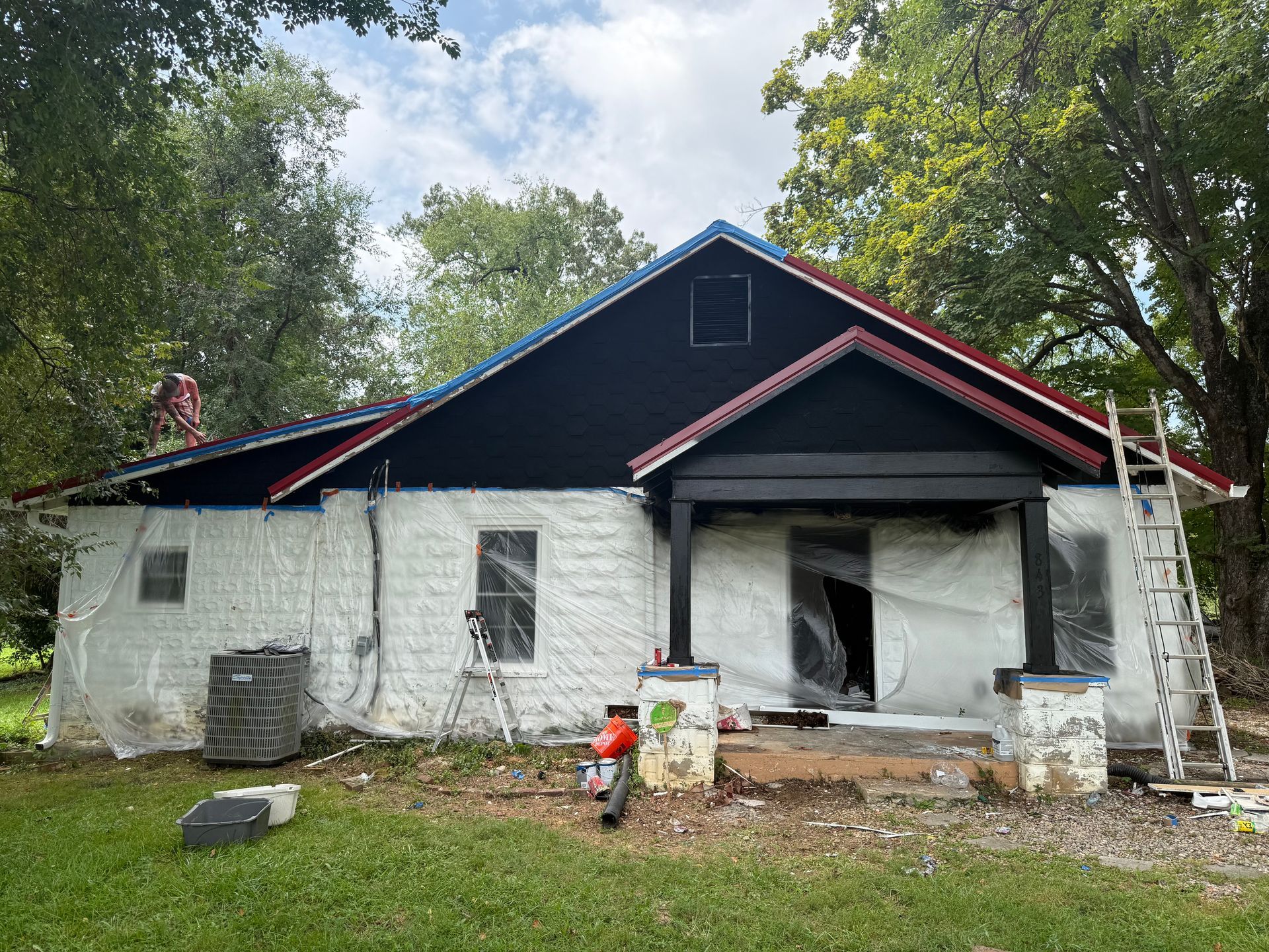 House exterior partially covered with white material for painting; black roof and trim.