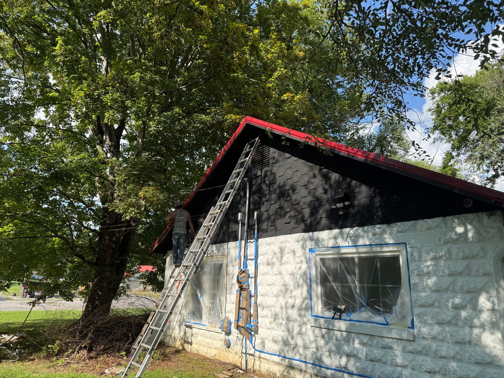 Exterior view of a small building being worked on; ladder leaning against the roof, charred facade, tape on the windows.