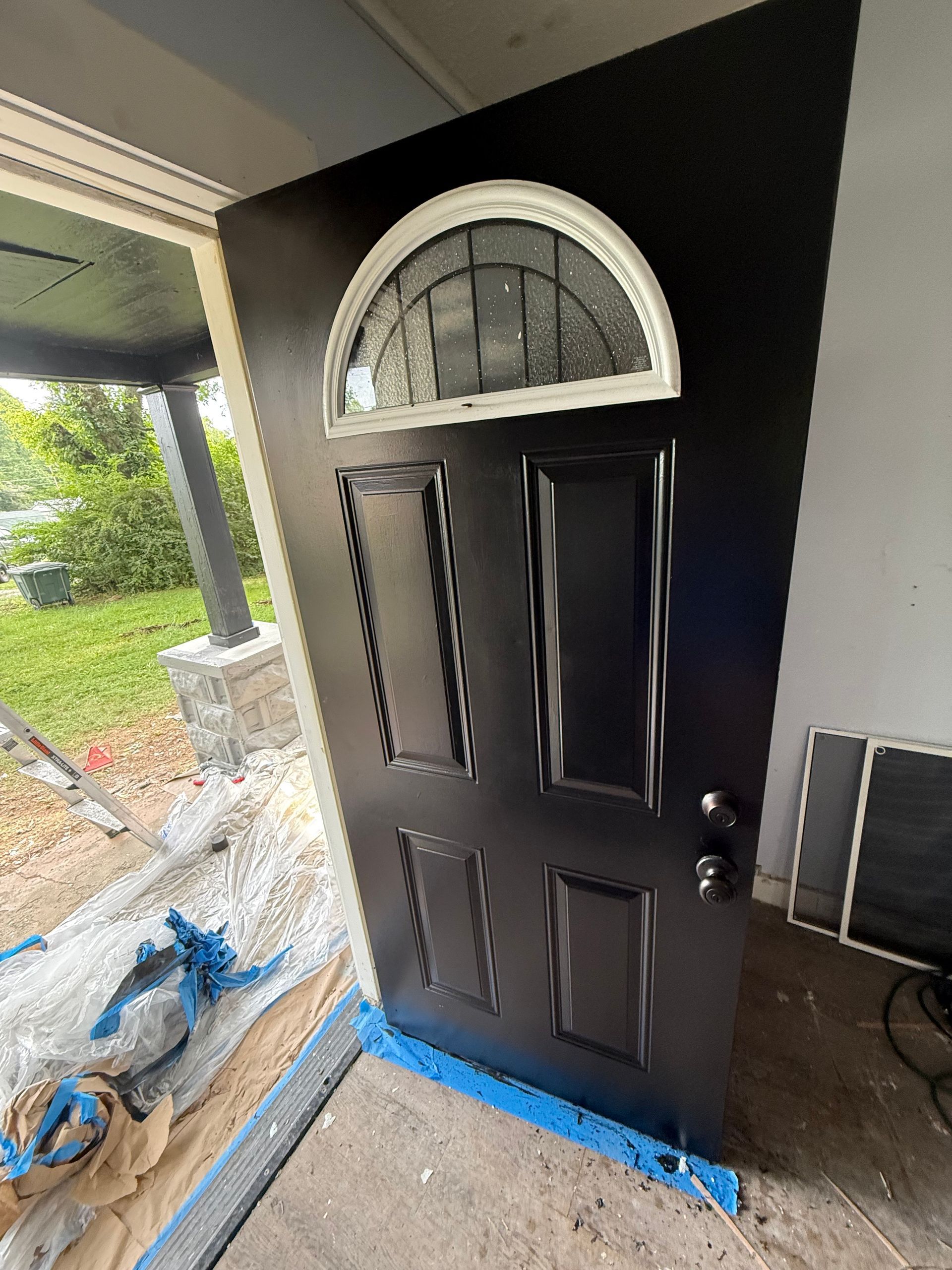 Black front door with a half-circle window, painted and ready to be installed in its frame.