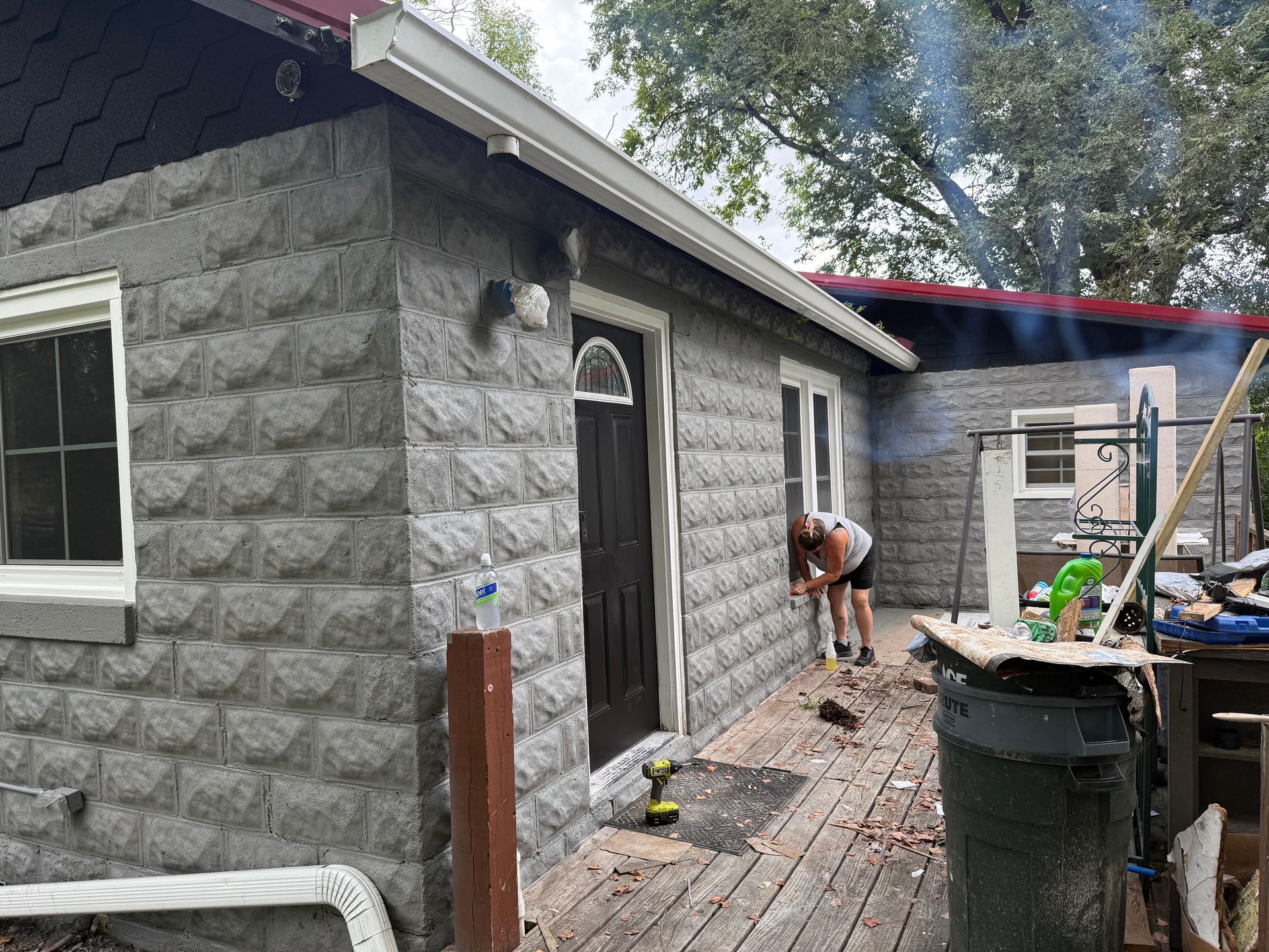 Gray brick-like siding on a house with a person working on the deck outside.