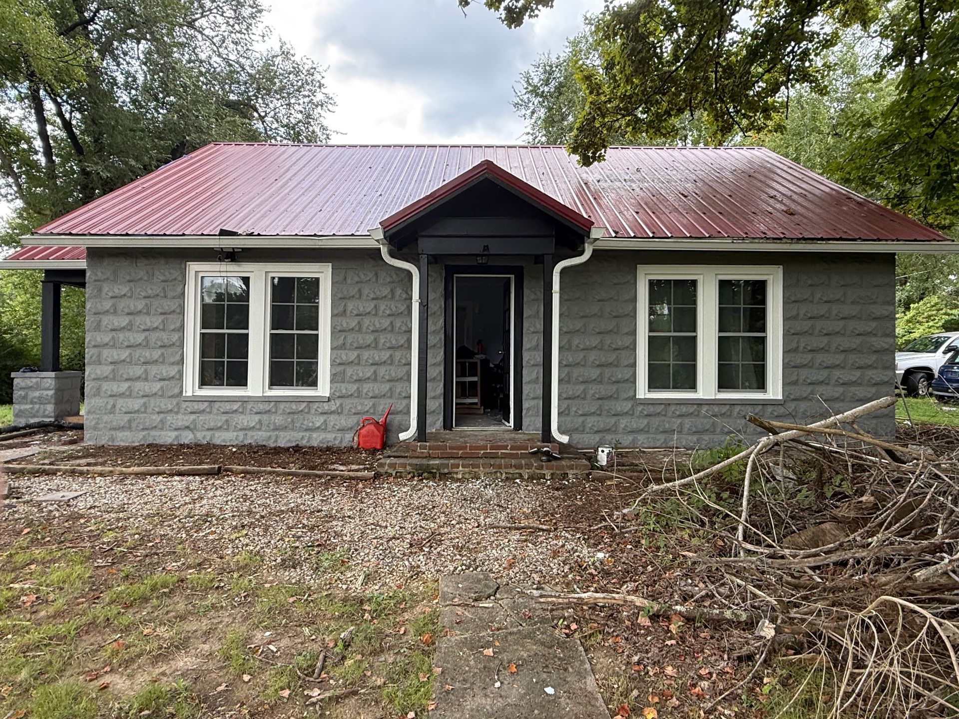Gray brick house with a red metal roof and white-framed windows. The front door is black.