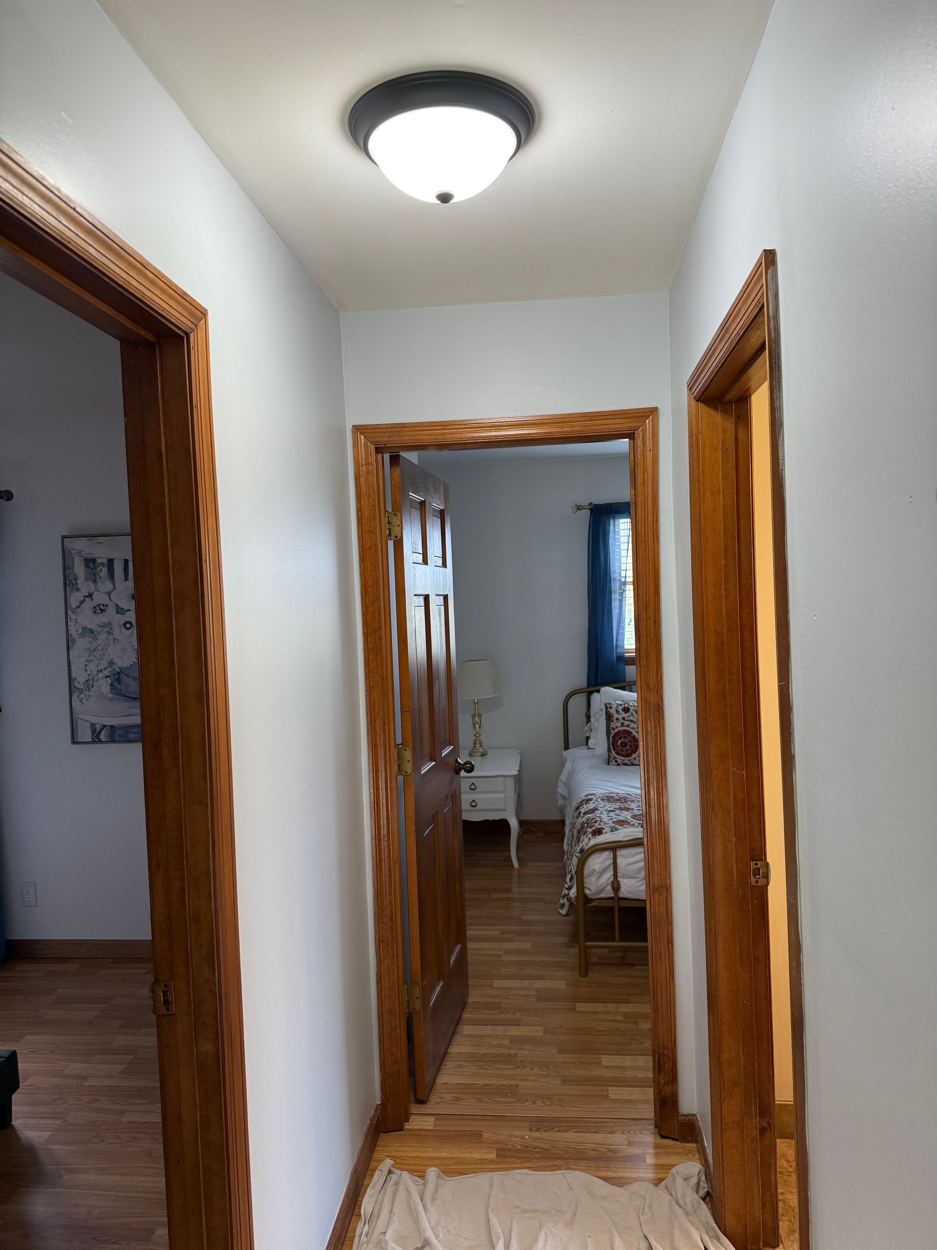 Hallway with three wooden door frames, a light fixture, and a view into a bedroom with a bed and window.