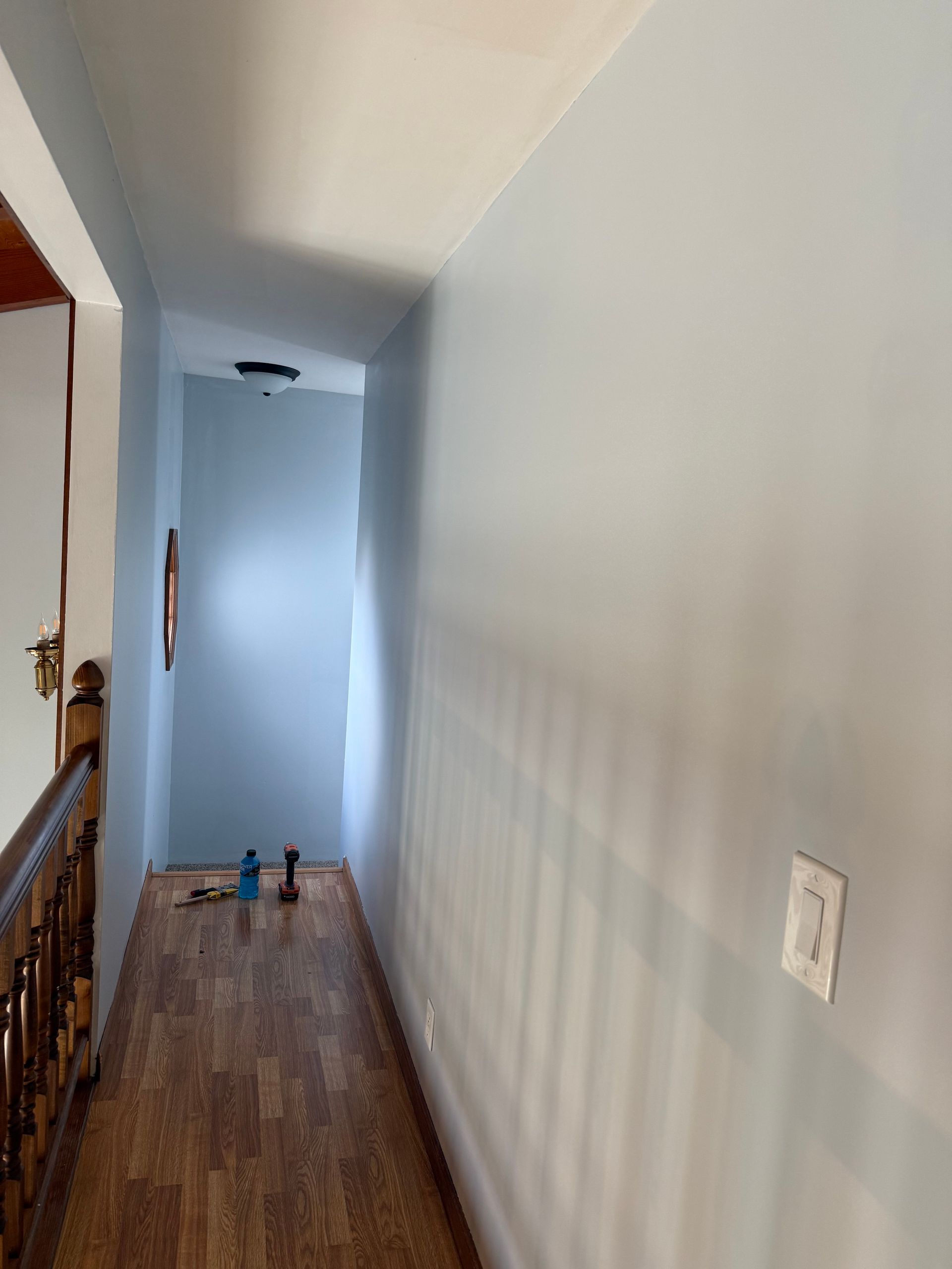 Narrow hallway with light blue walls, wooden floor, and a light switch.