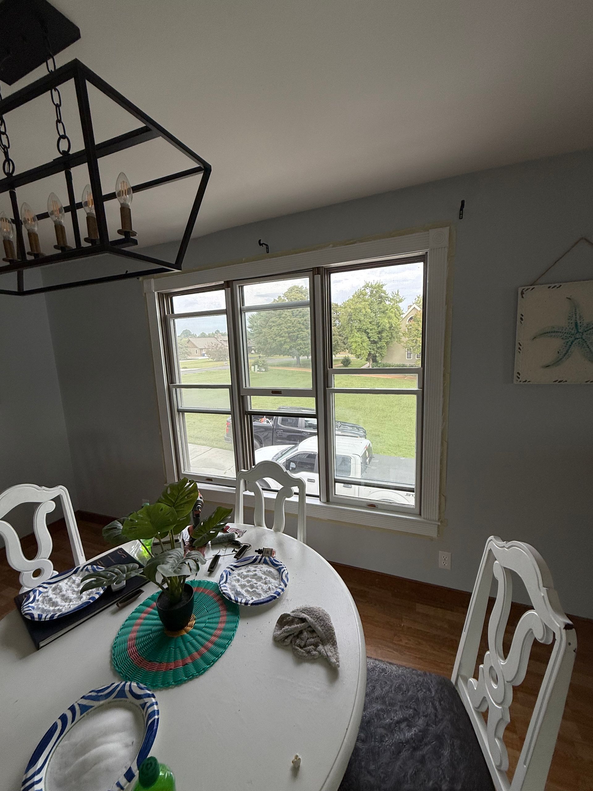 Dining room with round white table, chairs, and window overlooking a yard. A chandelier hangs above.