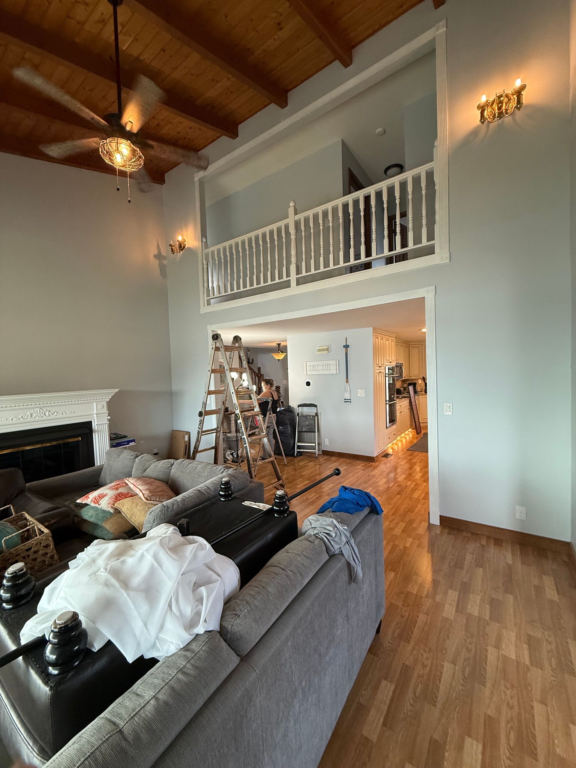 Living room with high ceiling, loft, and a sofa. Blue walls, wood floor and ceiling, white railing.