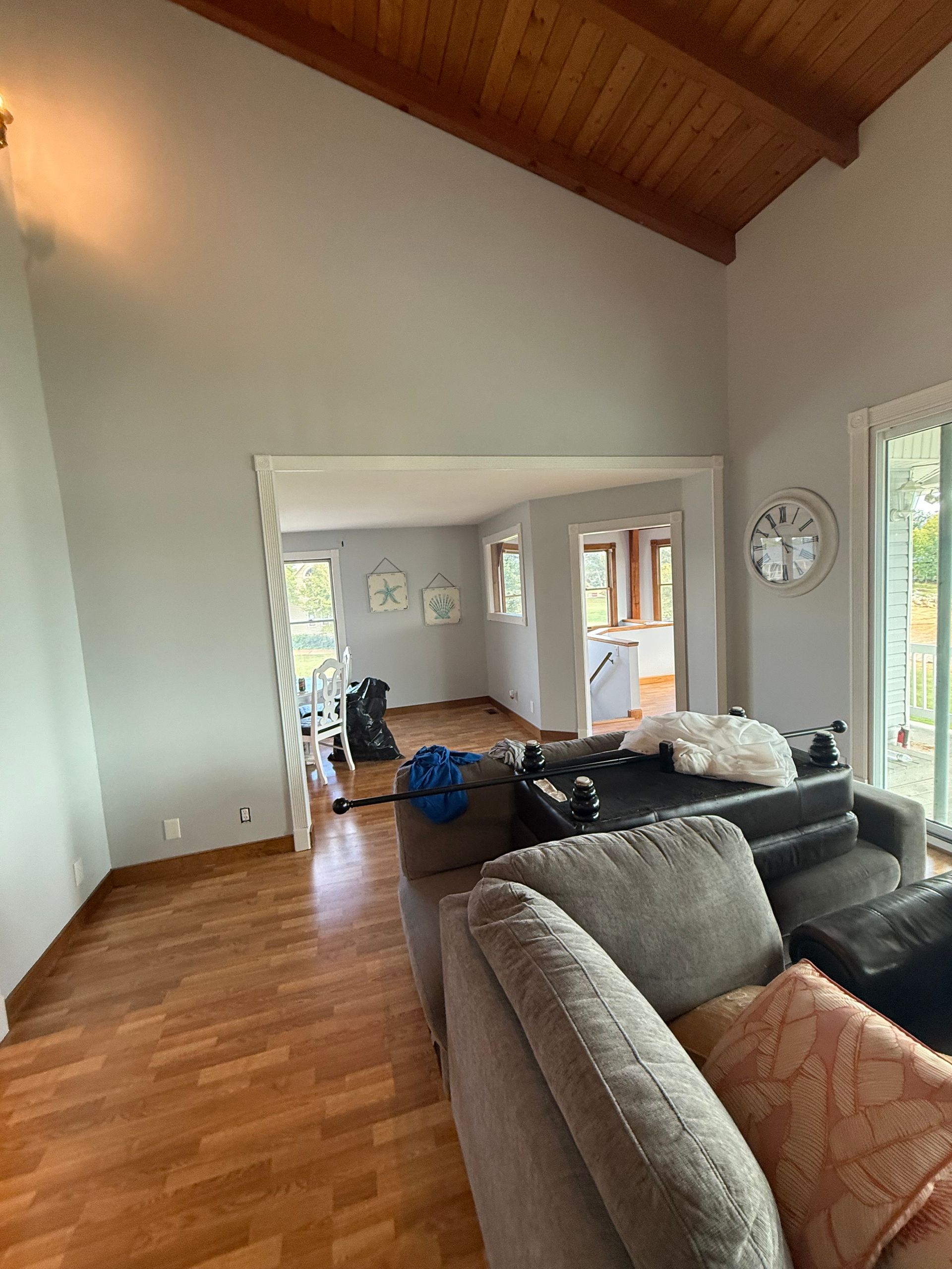 Living room with wood floors, gray walls, and exposed wood ceiling. Open doorway leads to another room.