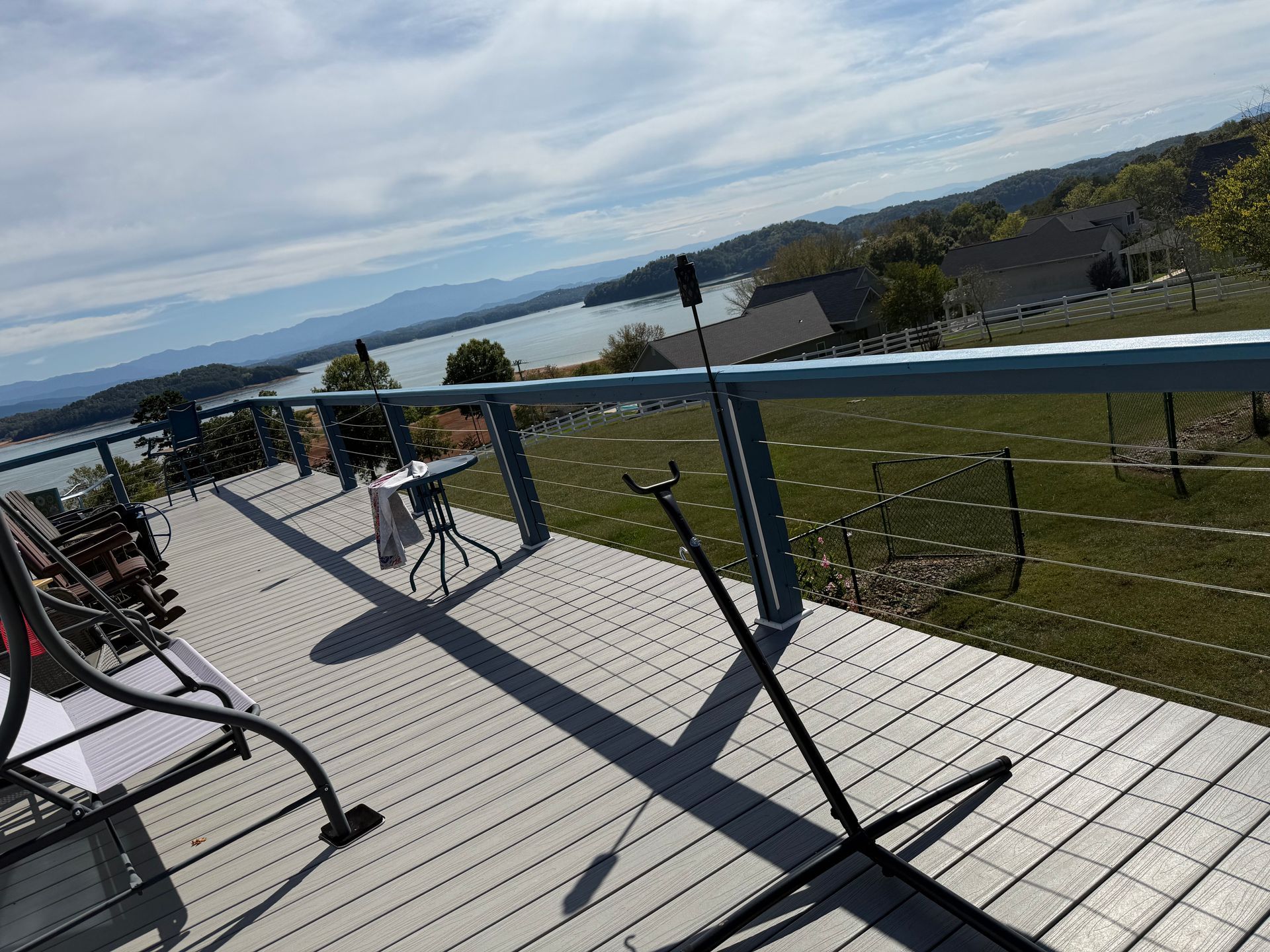 Deck overlooking lake and mountains; railing, tripod, and lawn visible.