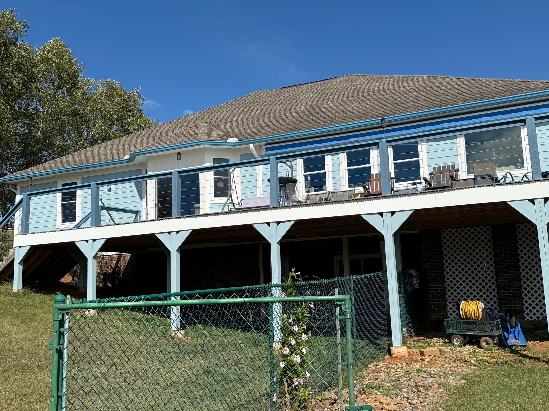 Blue house with a deck. Green fence in the foreground. Blue sky.