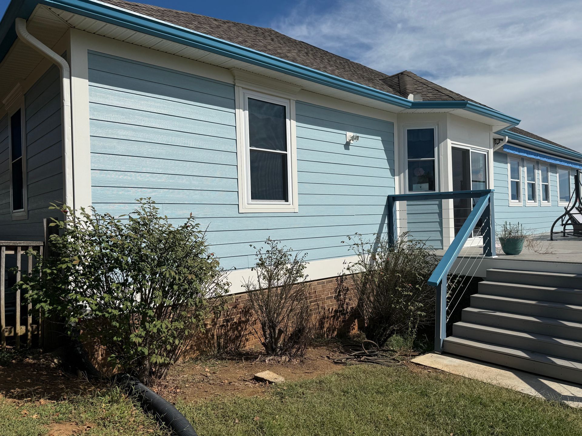 Blue house with white trim, windows, and a deck with stairs.