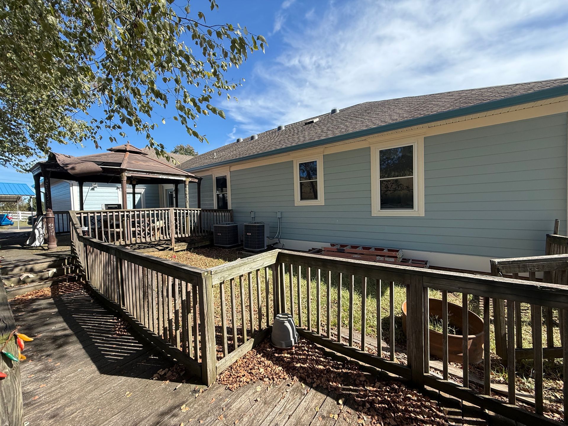 Back of house with a wooden ramp, deck, and gazebo; blue siding, blue sky.