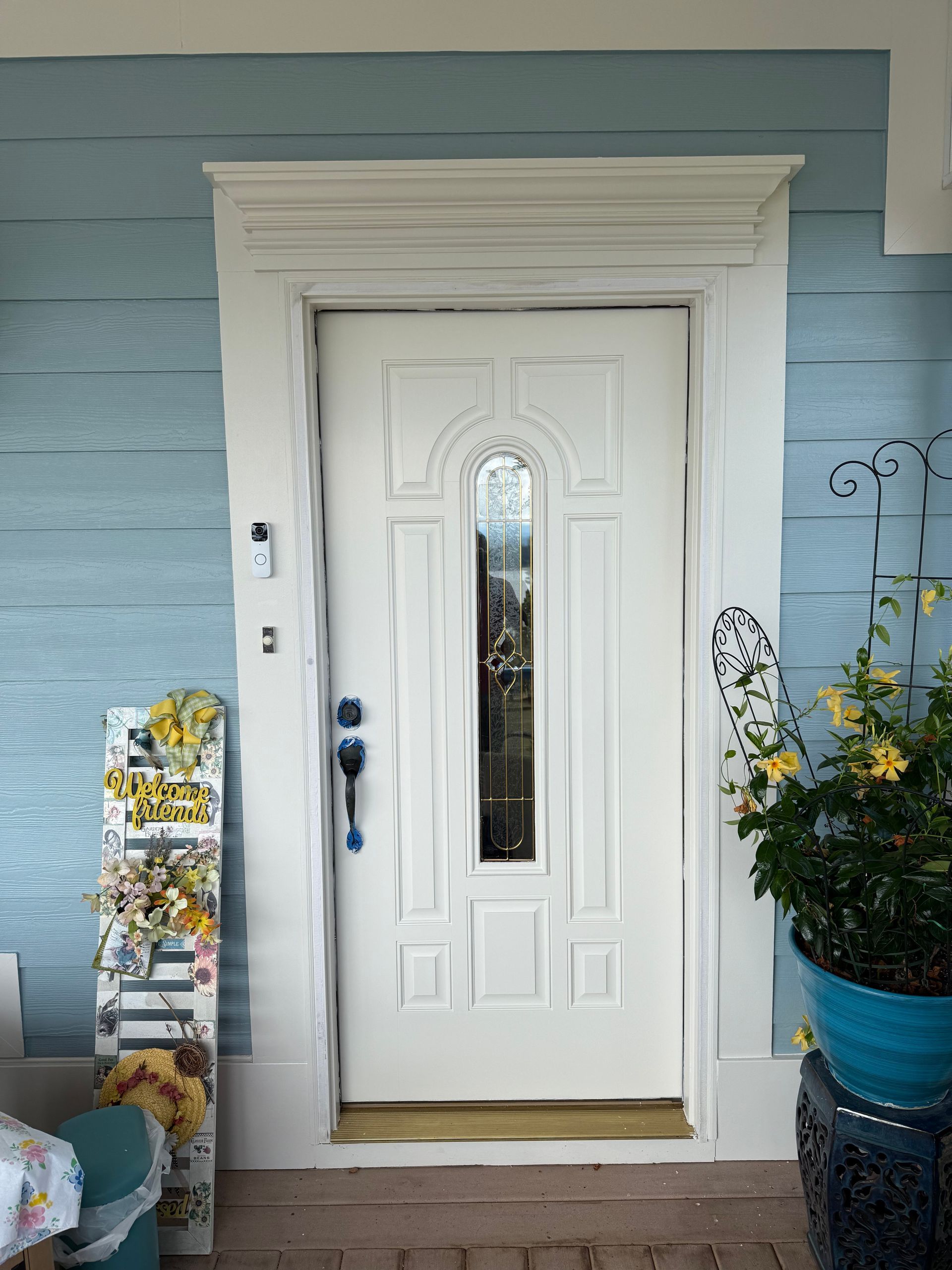 White front door with long glass panel and decorative trim, set in blue siding.