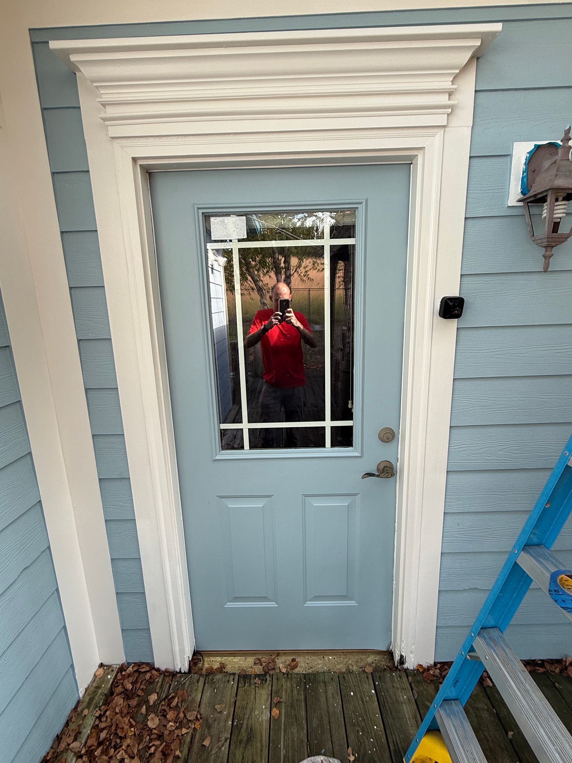Blue door with glass panel, white trim, and a person taking a photo in the reflection.