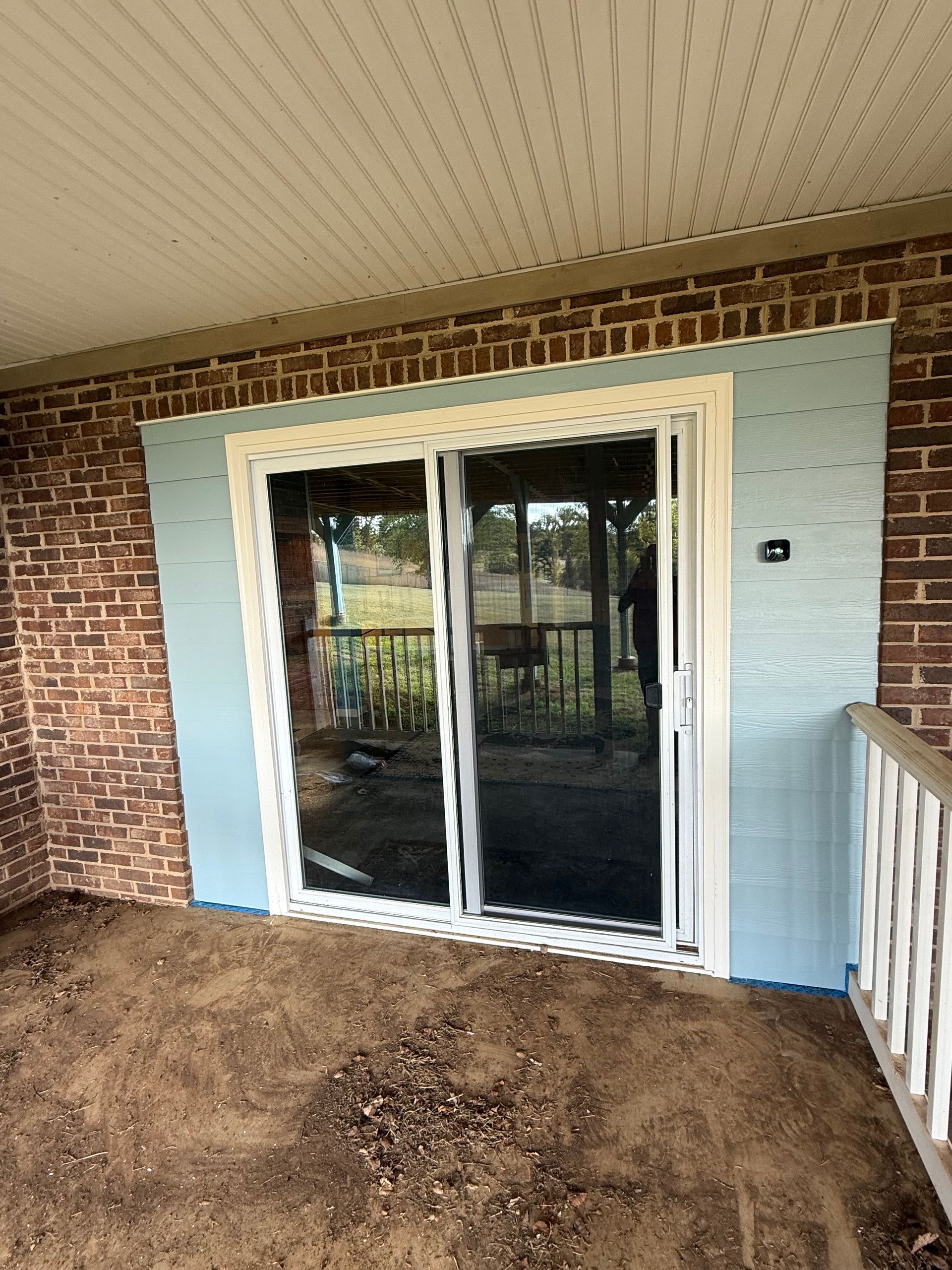 Sliding glass doors with white frame, light blue siding, brick wall.