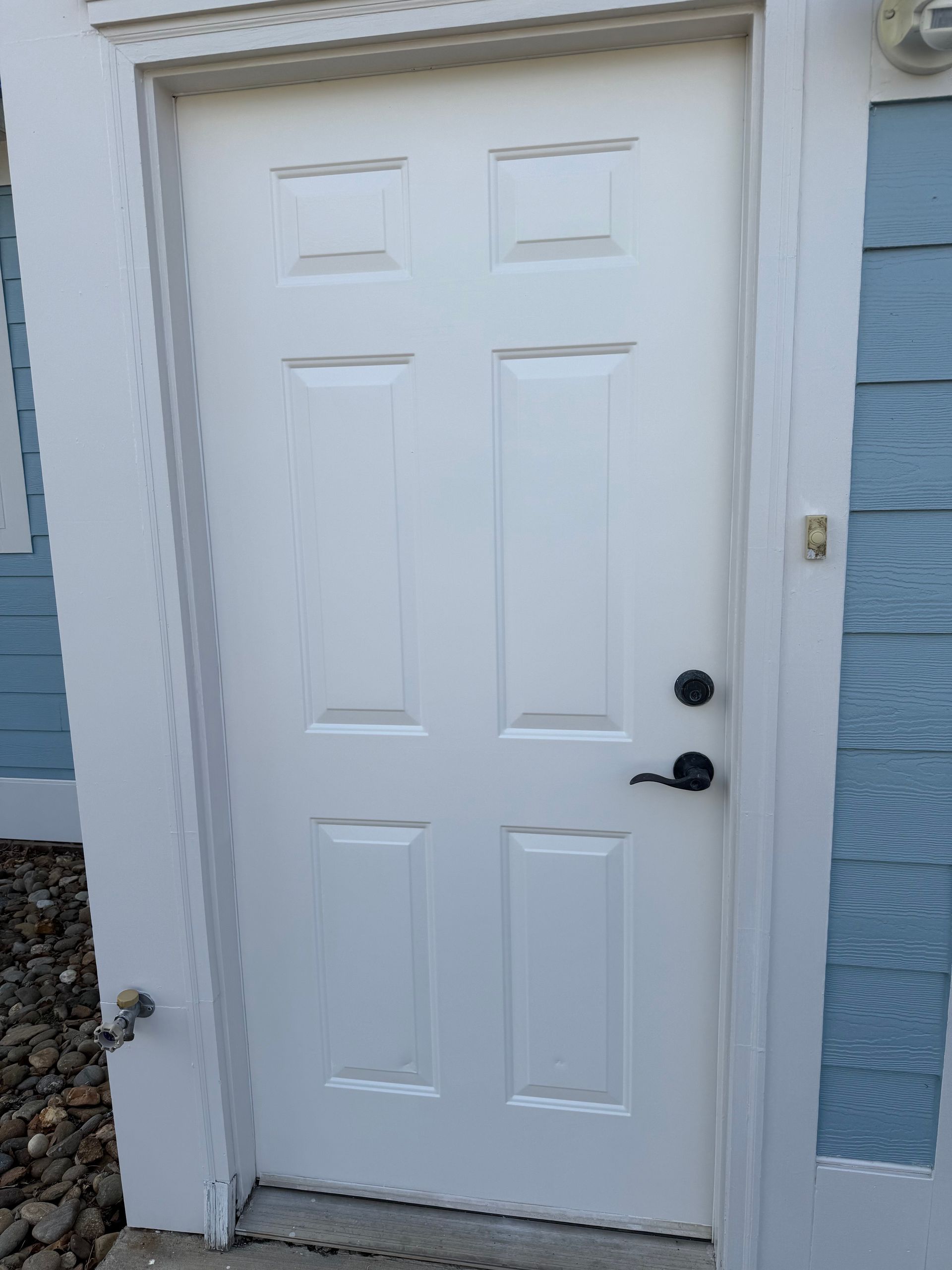 White exterior door with black hardware, next to blue siding and white trim.