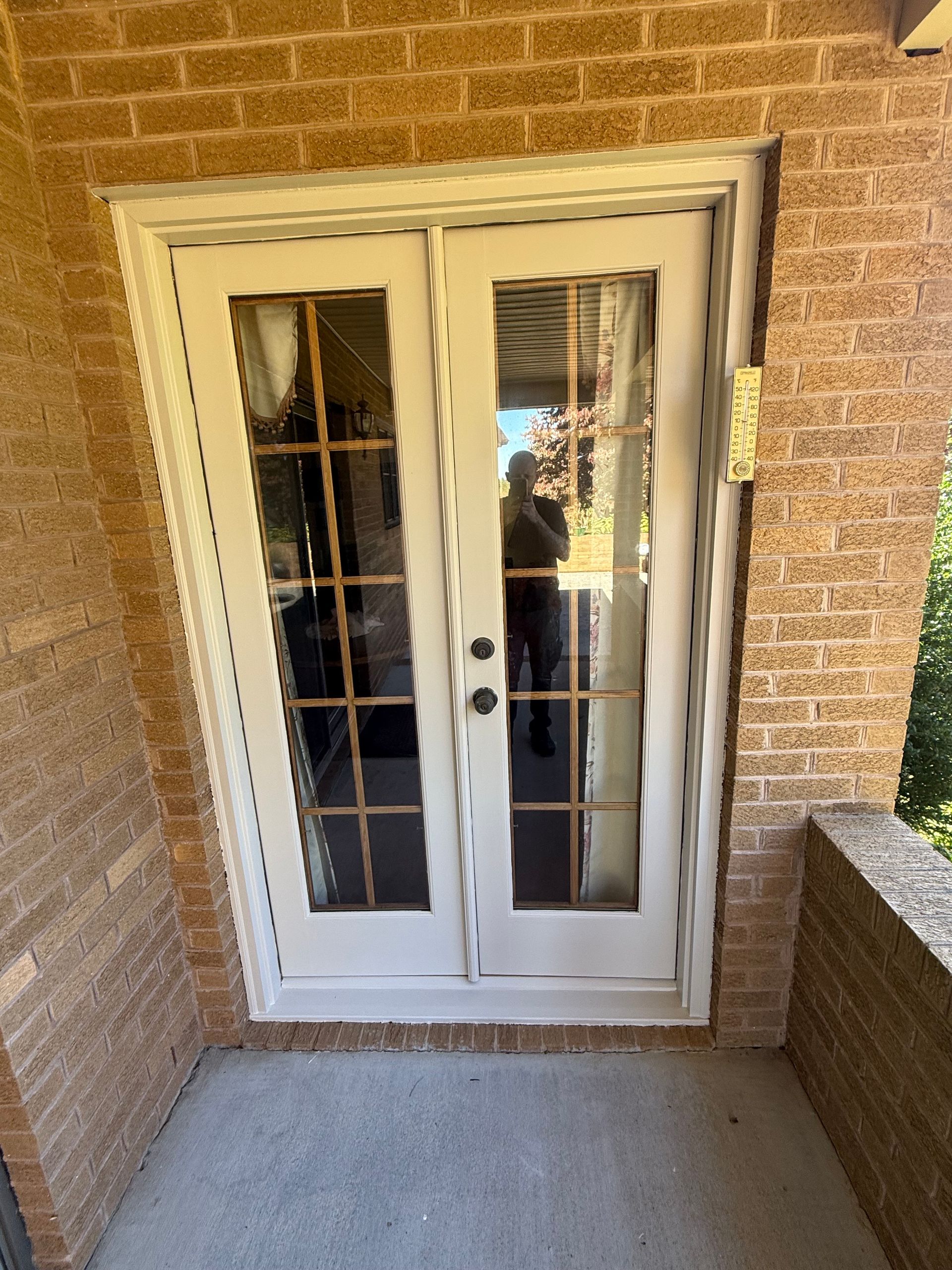 White French doors with multiple panes, set in a brick wall. A person is visible in the reflection.