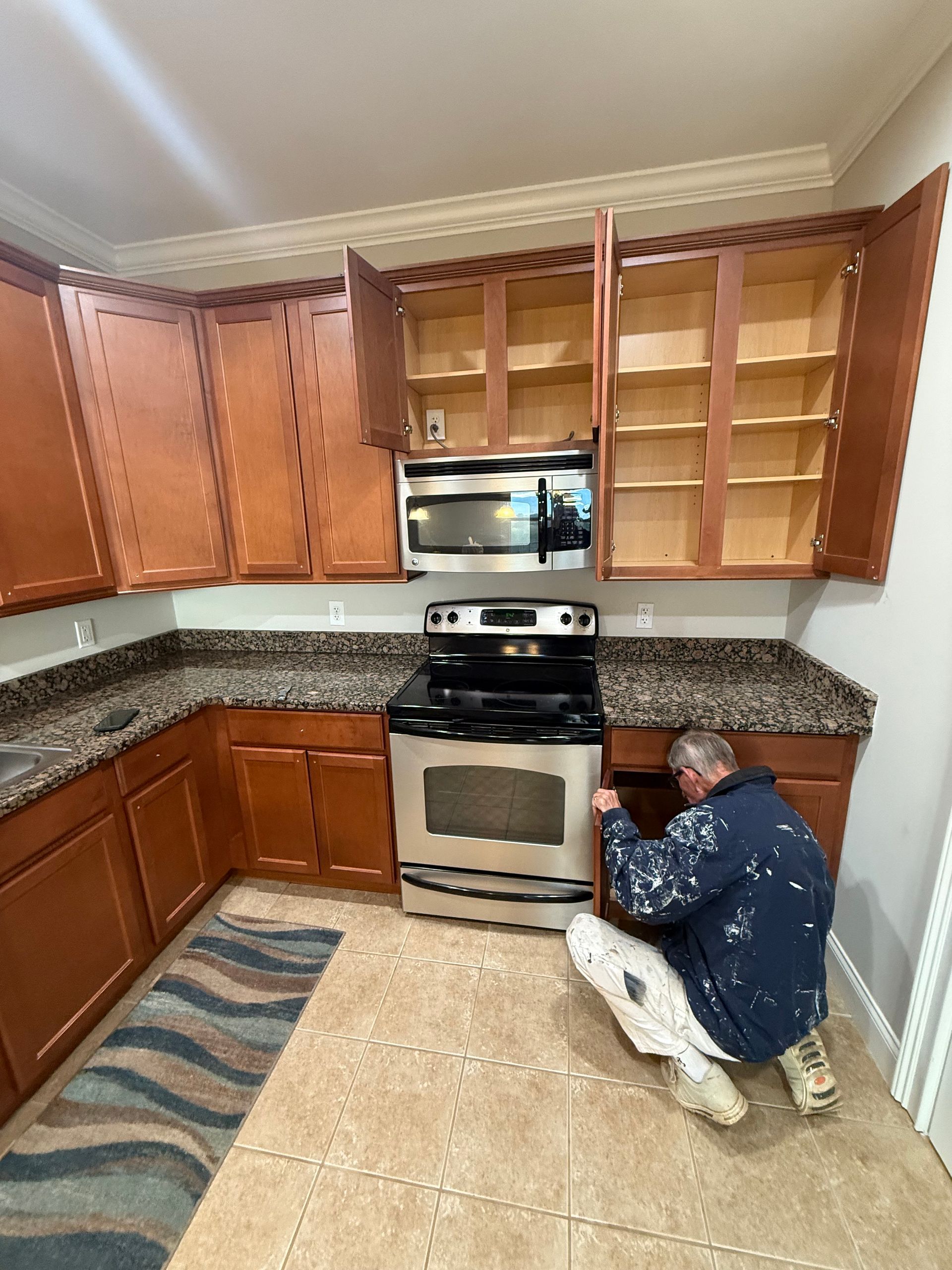 Kitchen with brown cabinets, a stove, and a person working on a cabinet.