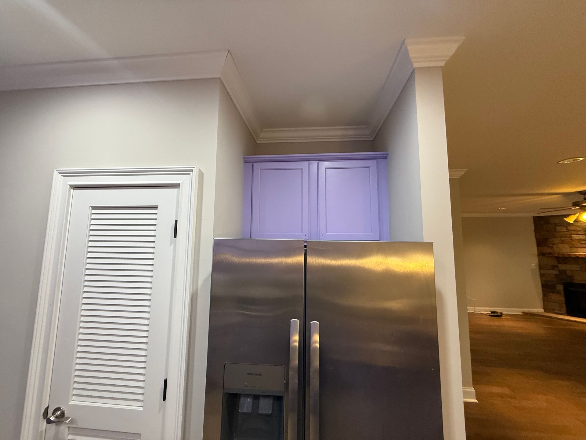 Stainless steel refrigerator with lavender cabinets above, next to a white door.