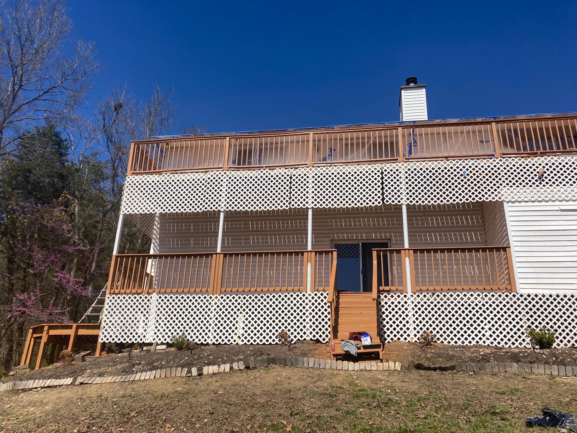Brown and white house with lattice exterior and deck against a clear blue sky.
