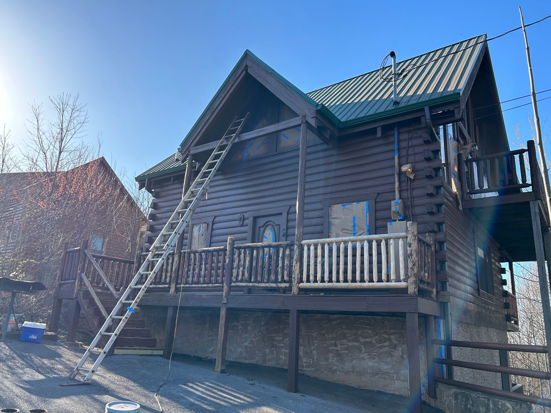 Log cabin with a ladder leaning against the roof, front porch with a railing, and blue sky.