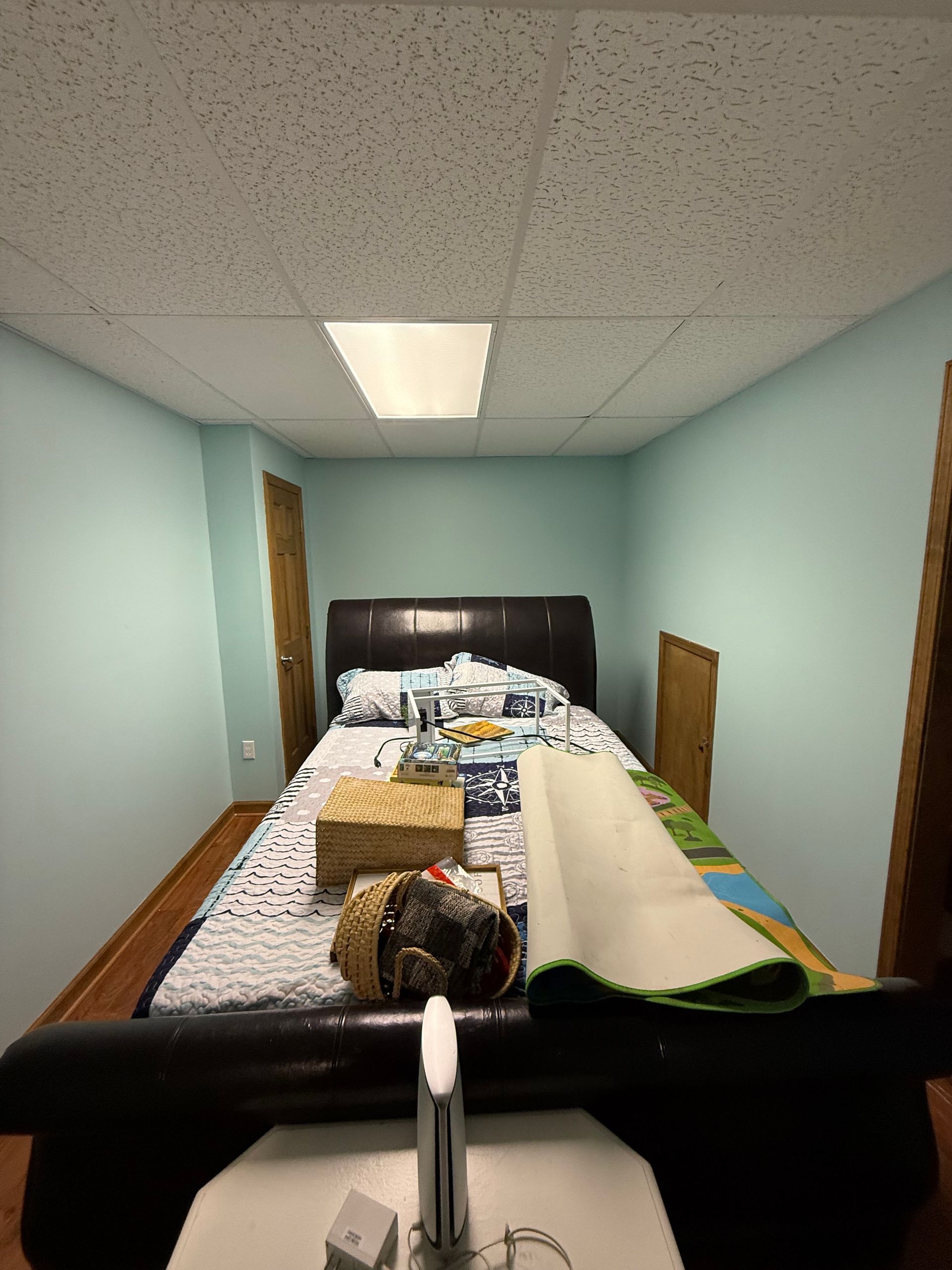 Bedroom with bed, basket, and items on the bed, light blue walls, and a dropped ceiling.