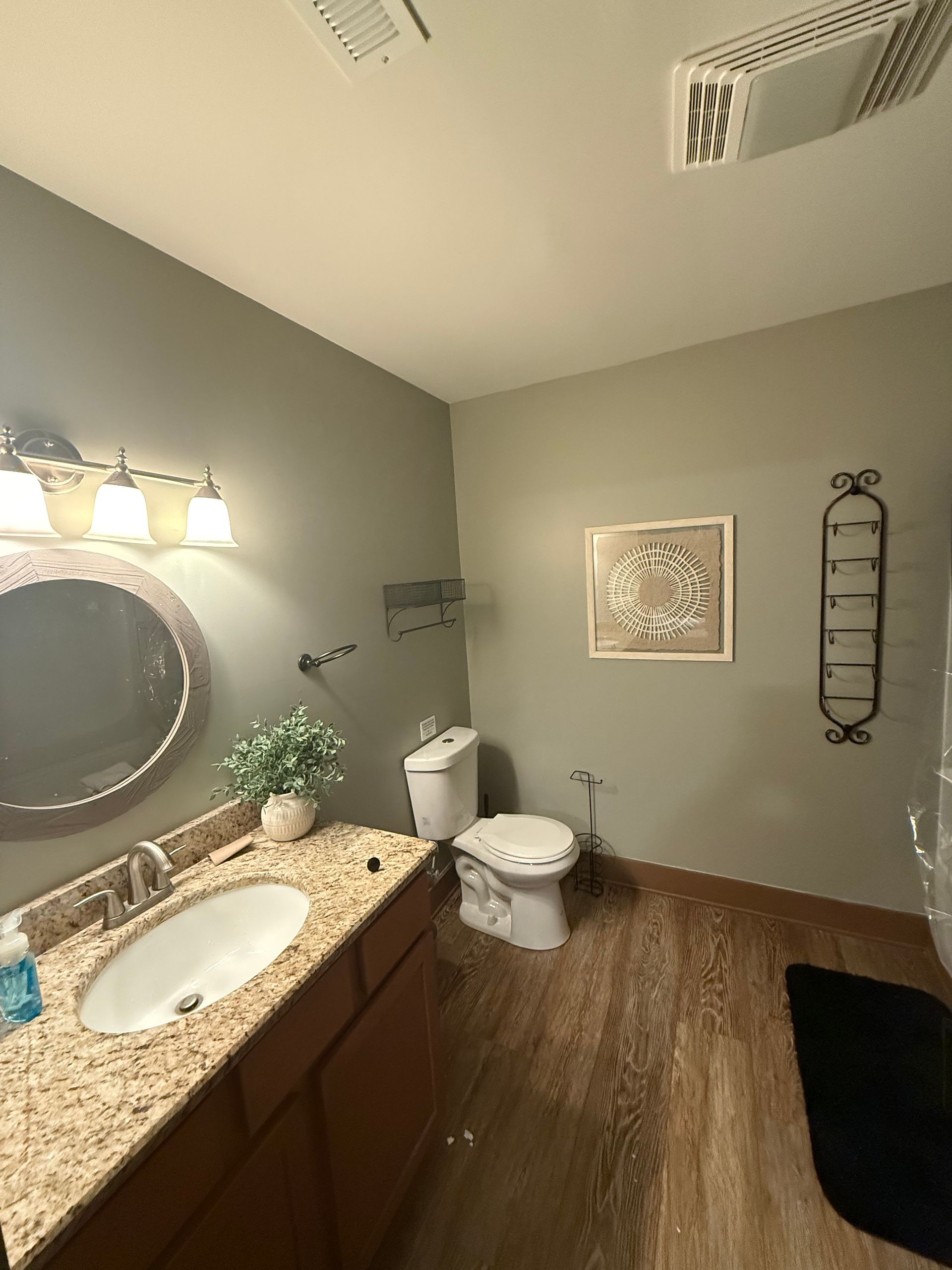 Bathroom with a vanity, toilet, and accessories on a brown floor and gray walls.