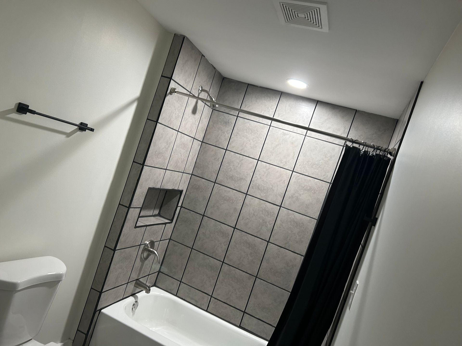 Bathroom with gray tile shower surround, black shower curtain, and a white toilet.