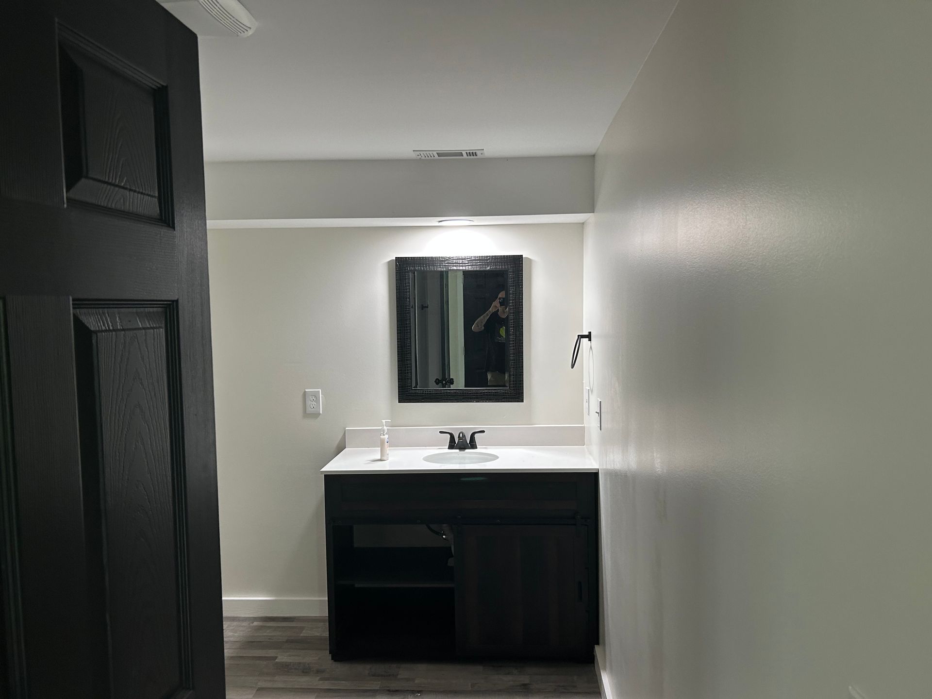 Bathroom with black vanity, mirror, and door. Gray walls and flooring.