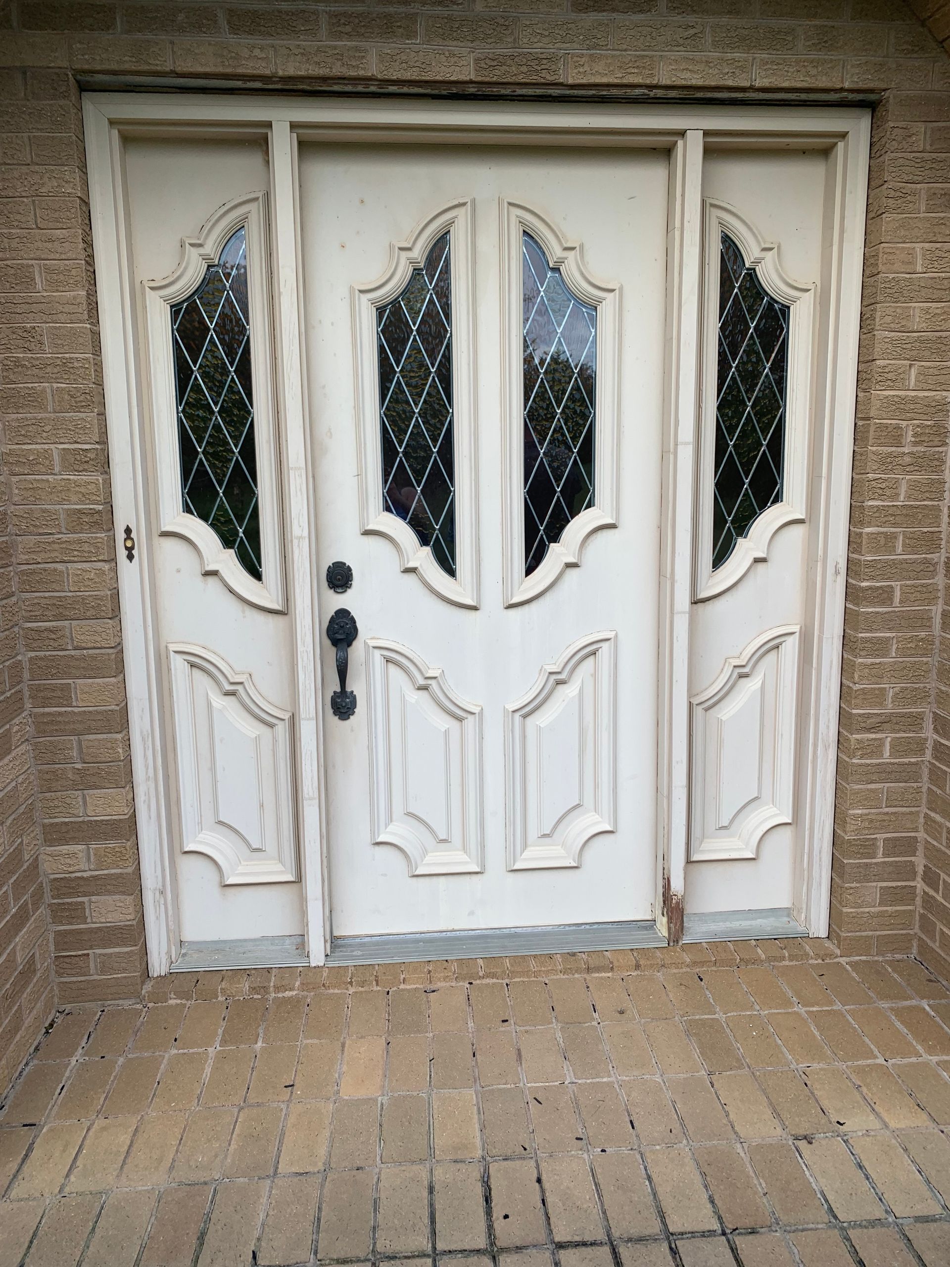 Cream-colored front door with sidelights, featuring diamond-paned glass and ornate molding, set in a brick facade.