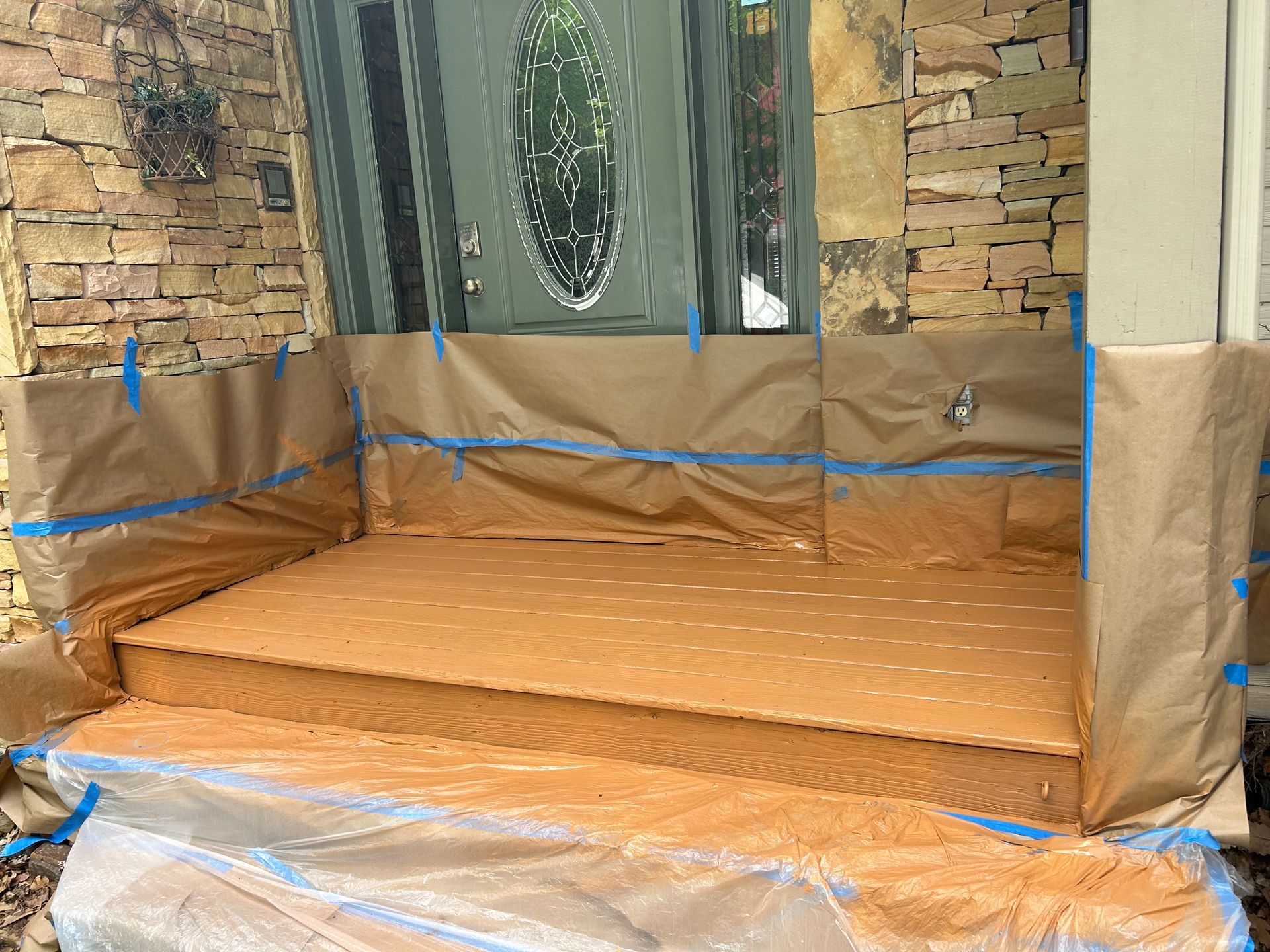 Exterior steps covered in brown paper and plastic, ready for painting. Blue tape protects surrounding areas.