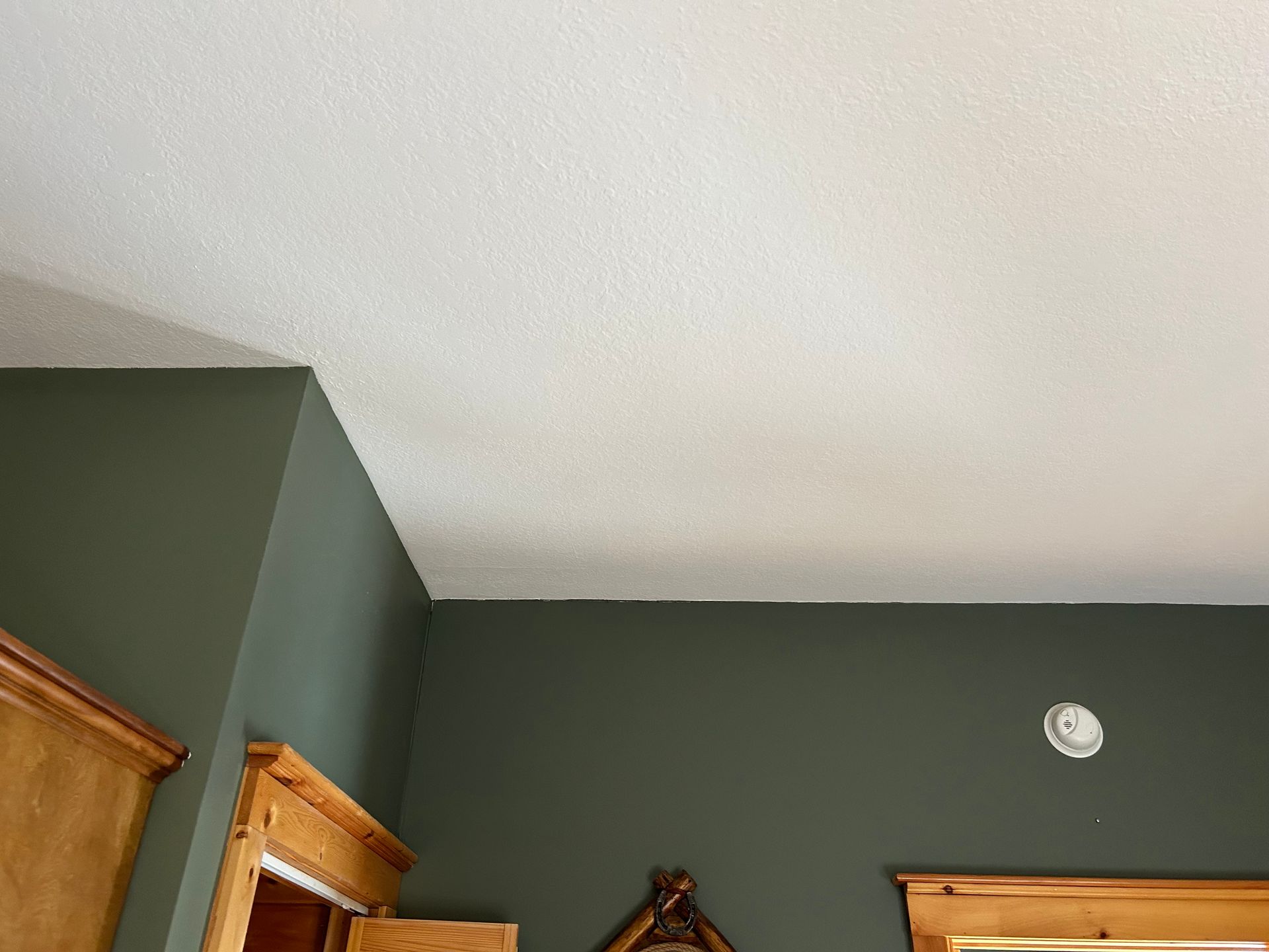 Corner of a room with green walls, a white textured ceiling, and wooden trim.