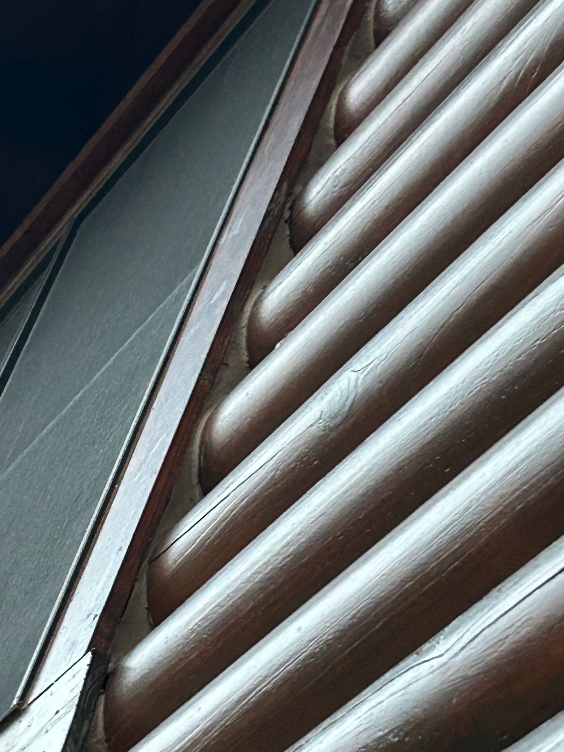 Angled close-up of brown, cylindrical wooden siding, adjacent to a dark, flat surface.
