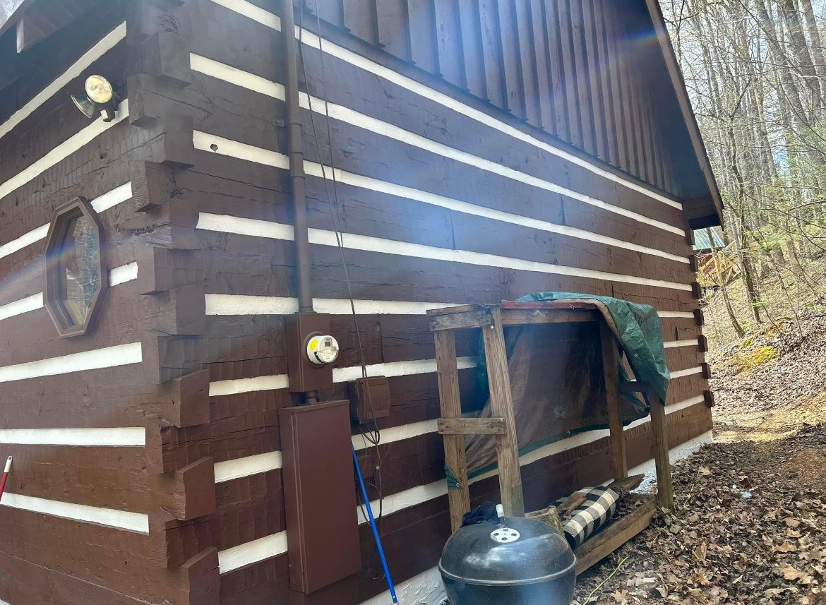 Brown cabin exterior with white stripes, smoker, and firewood storage.
