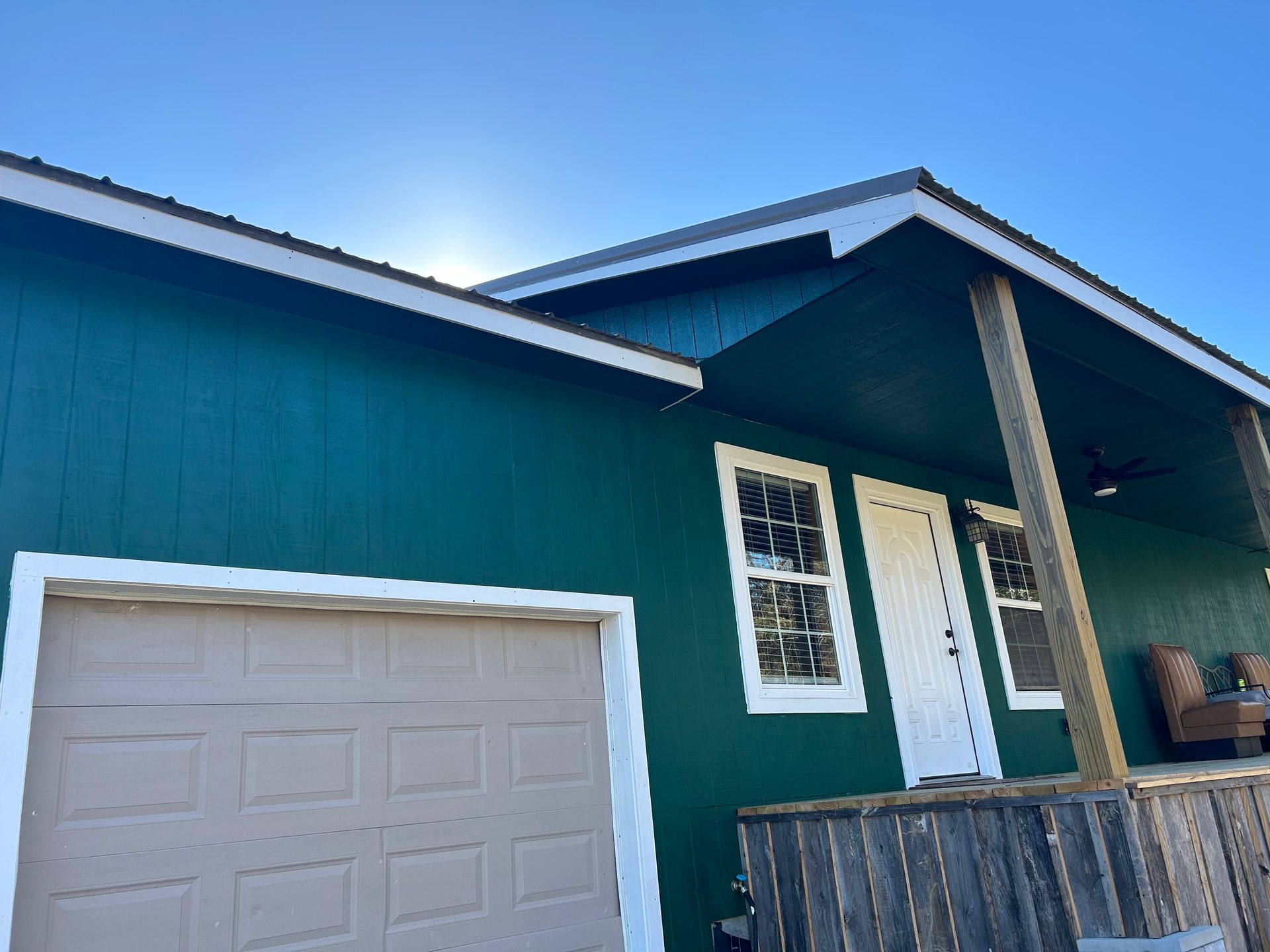 Green house with beige garage door and white trimmed windows and door under blue sky.
