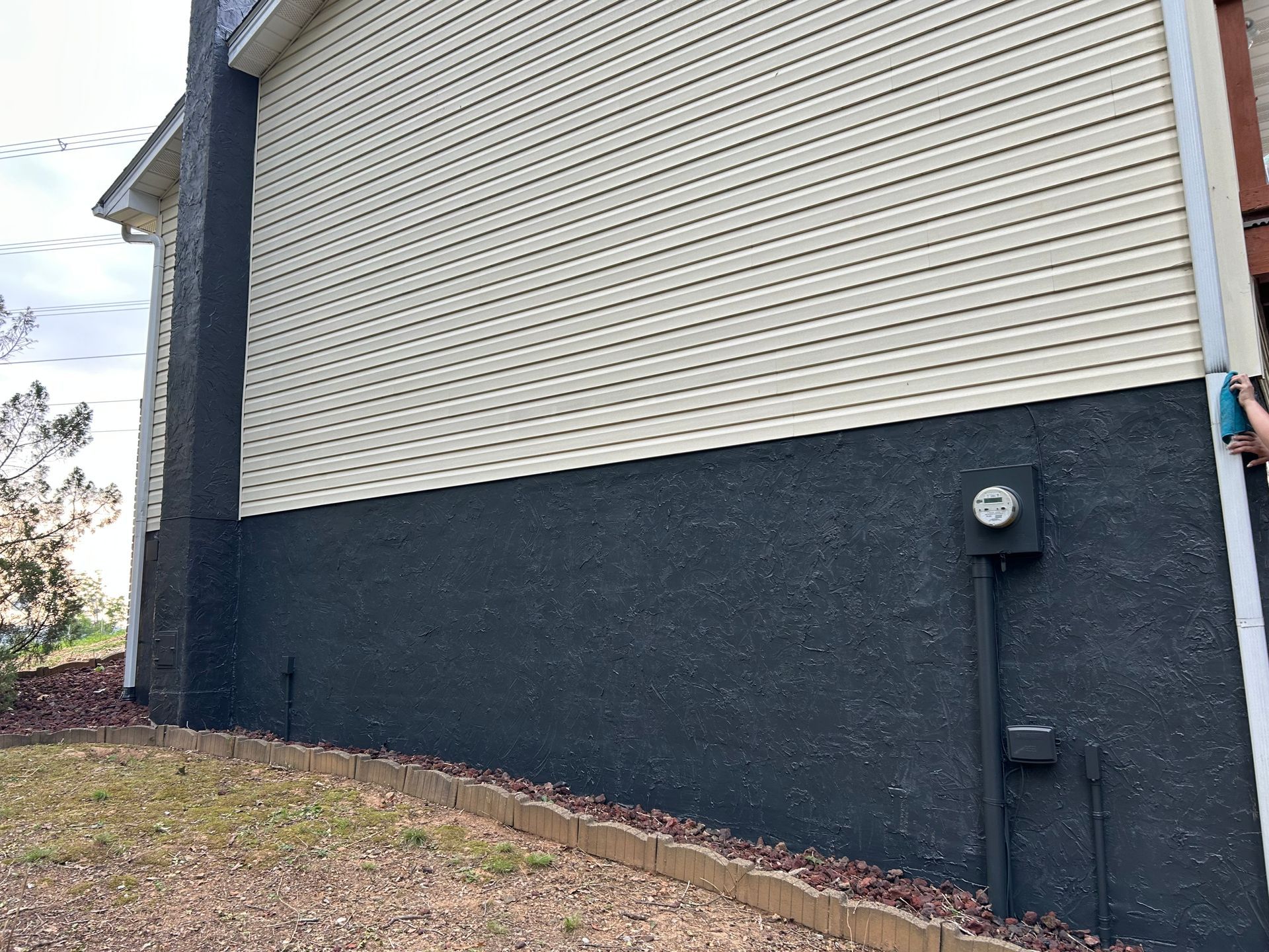 Black and beige house exterior with electrical box. Dark lower section, light upper section, chimney, and siding.