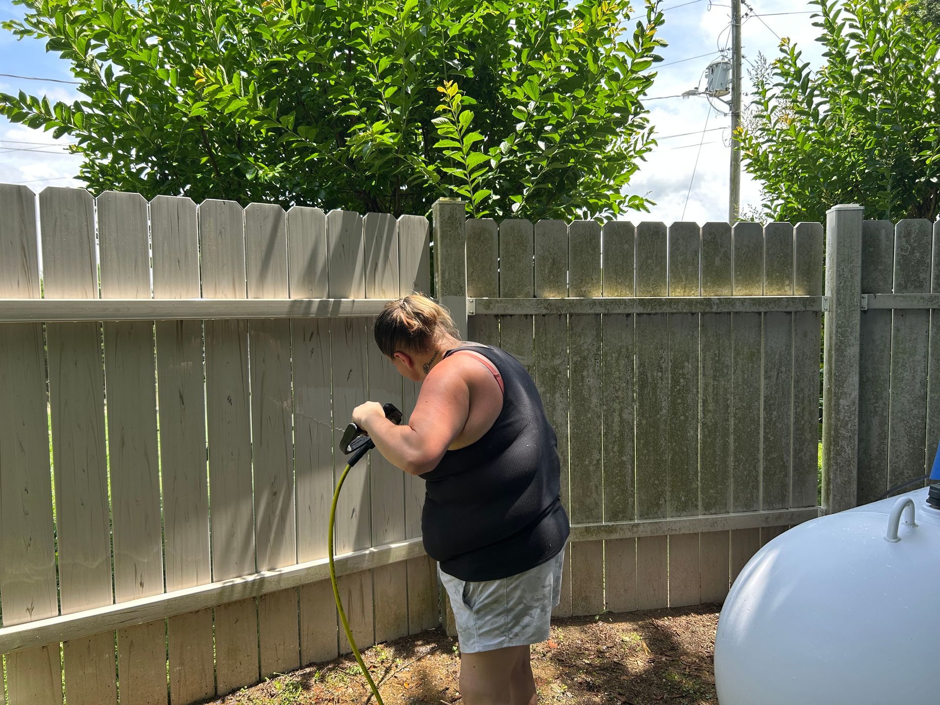 Person power washing a weathered wooden fence outdoors.