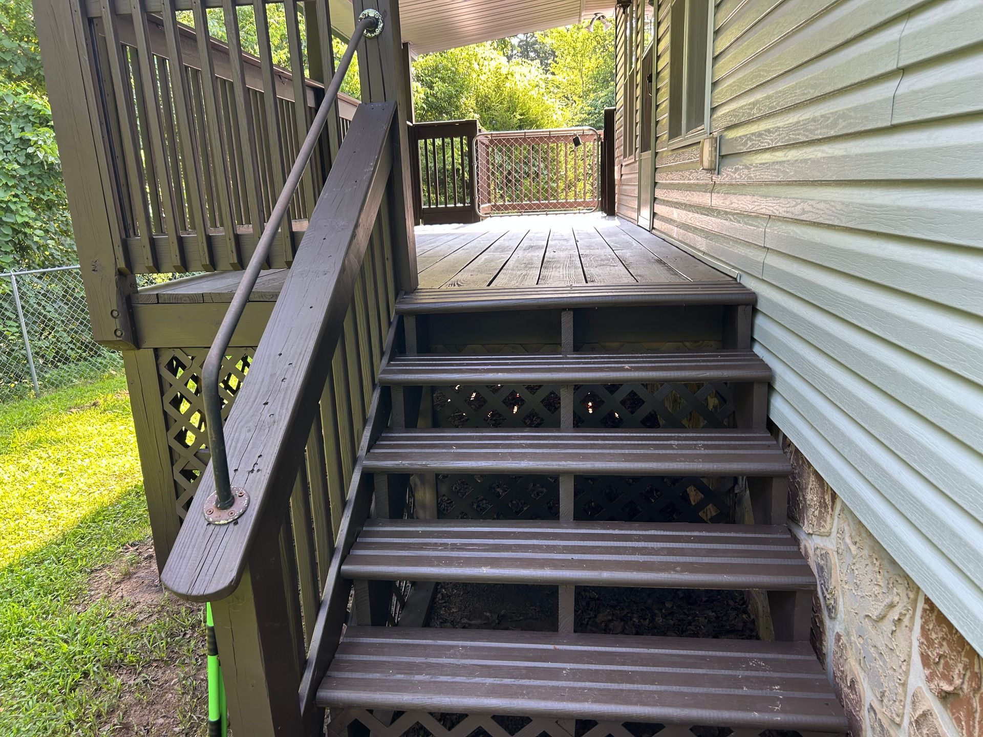 Brown wooden deck with steps leading up from a yard. A handrail and lattice details are visible.