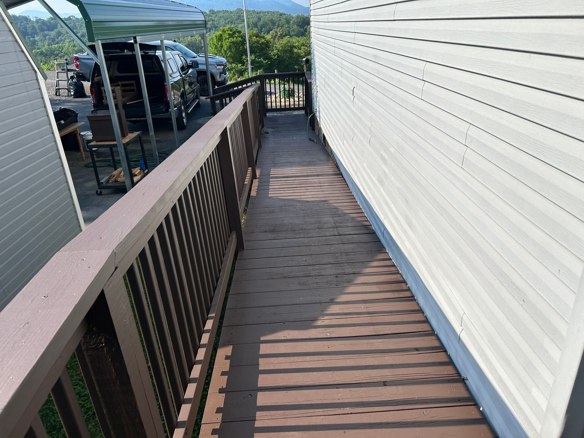Wooden deck walkway beside a white-sided building with brown railing and outdoor setting.