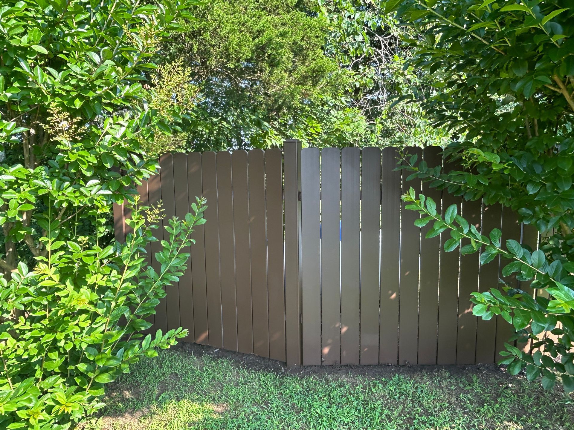 Brown wooden fence surrounded by green bushes and grass.